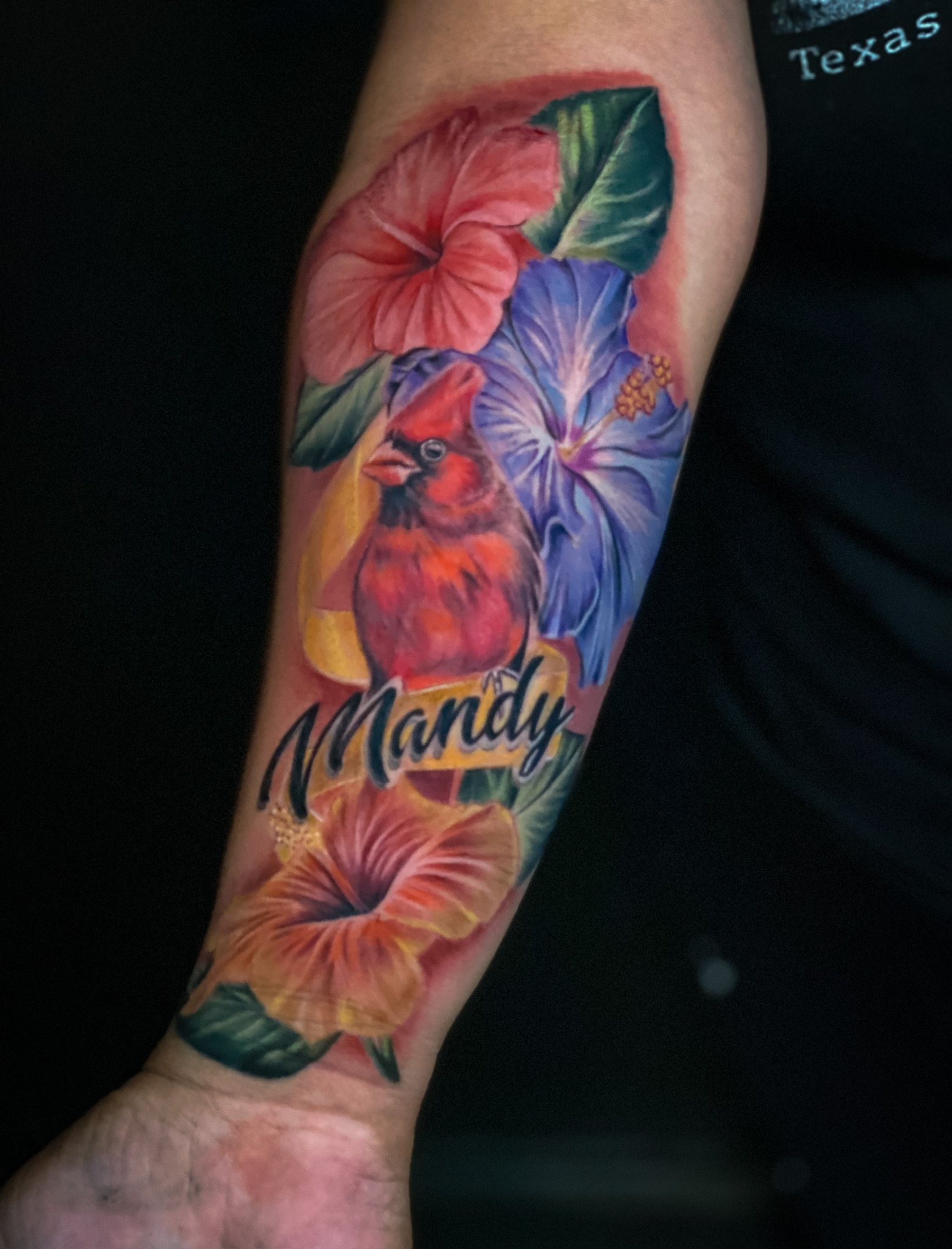 Colorful tattoo on an arm featuring a red bird, pink and purple hibiscus flowers