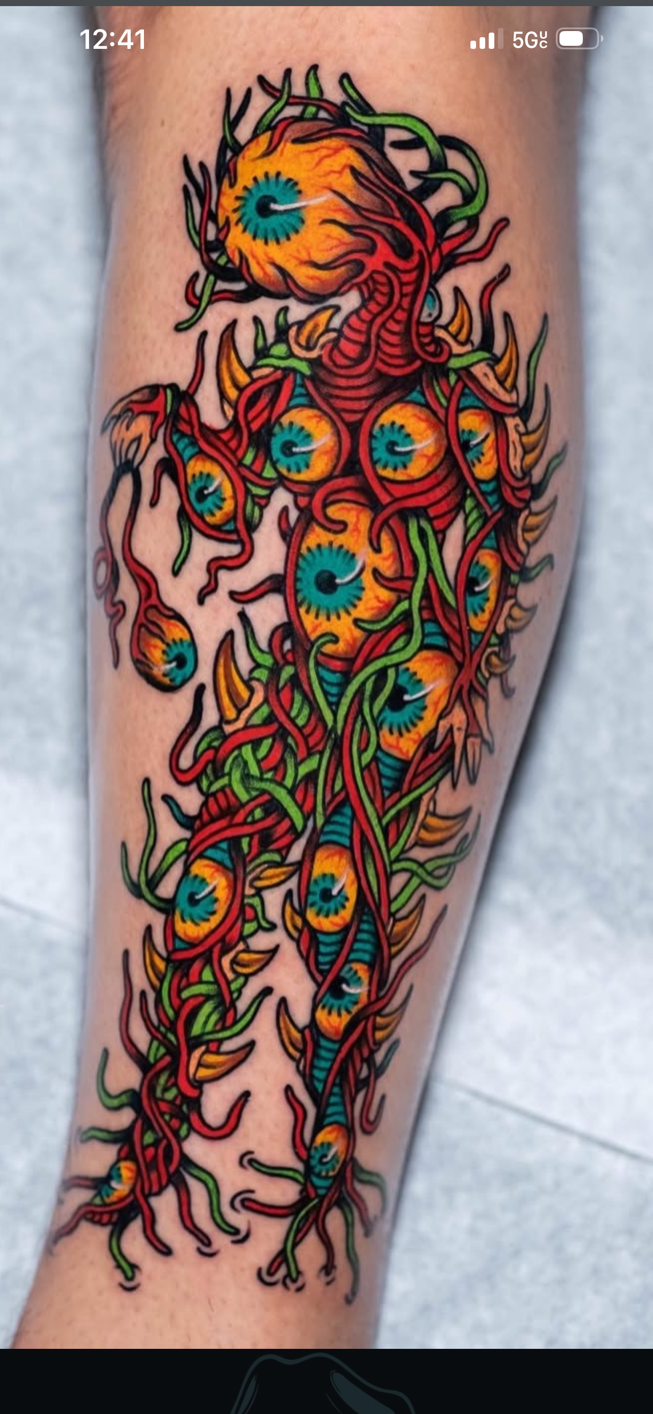 A colorful tattoo of multiple eyeballs with orange and blue irises, surrounded by red and green tentacle-like tendrils on a person's arm.