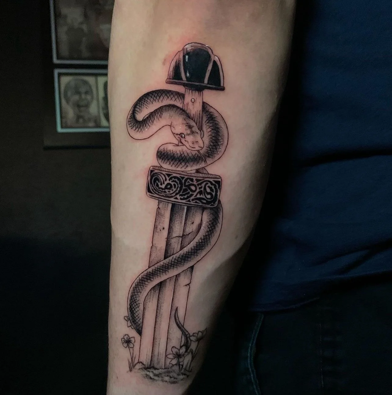 Tattoo of a snake wrapped around a wooden stake with a firefighter helmet on top, and a decorative band around the stake.
