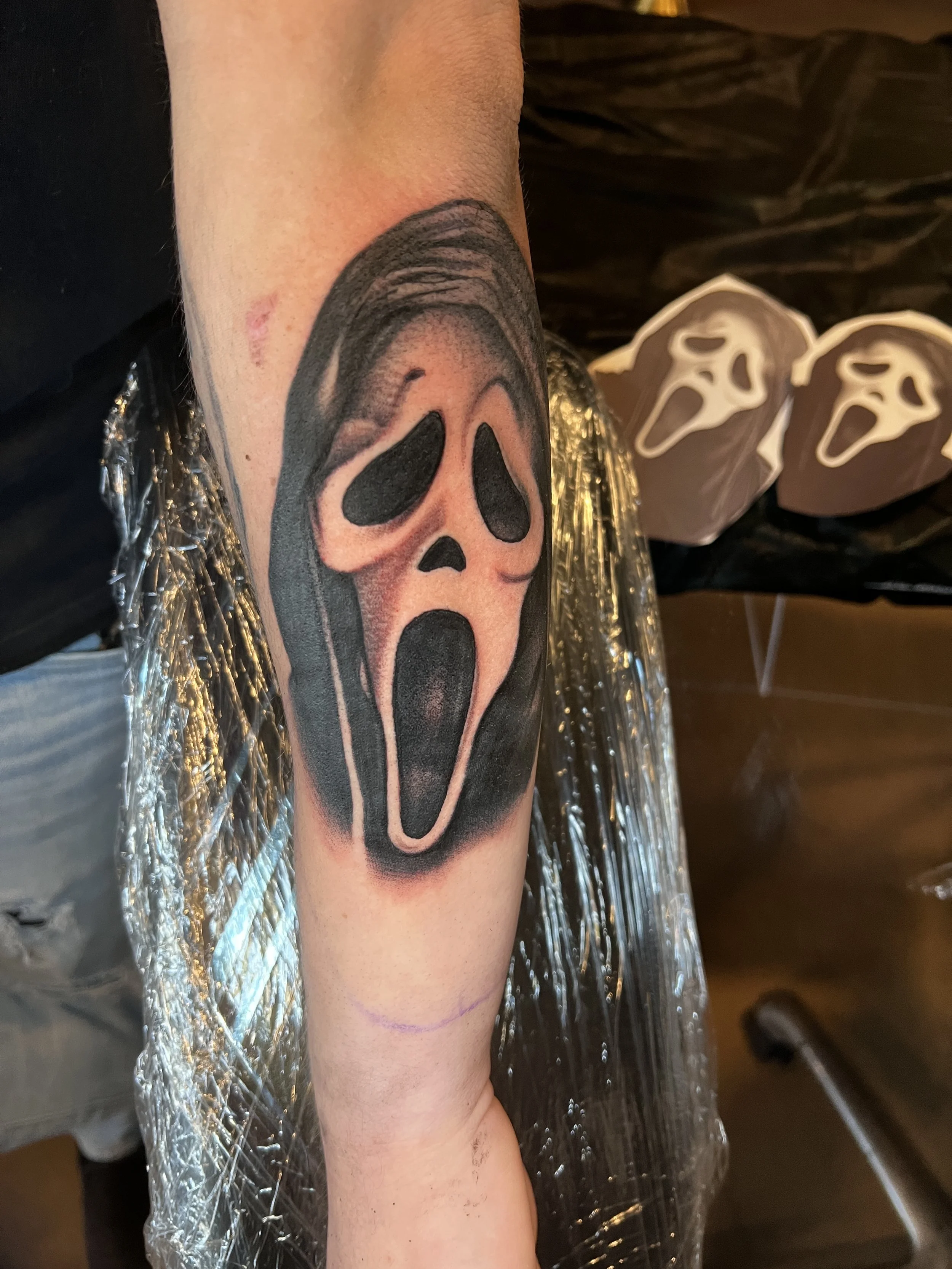 a black and grey portrait tattoo of the Scream character from the Scream movie franchise on a person's forearm