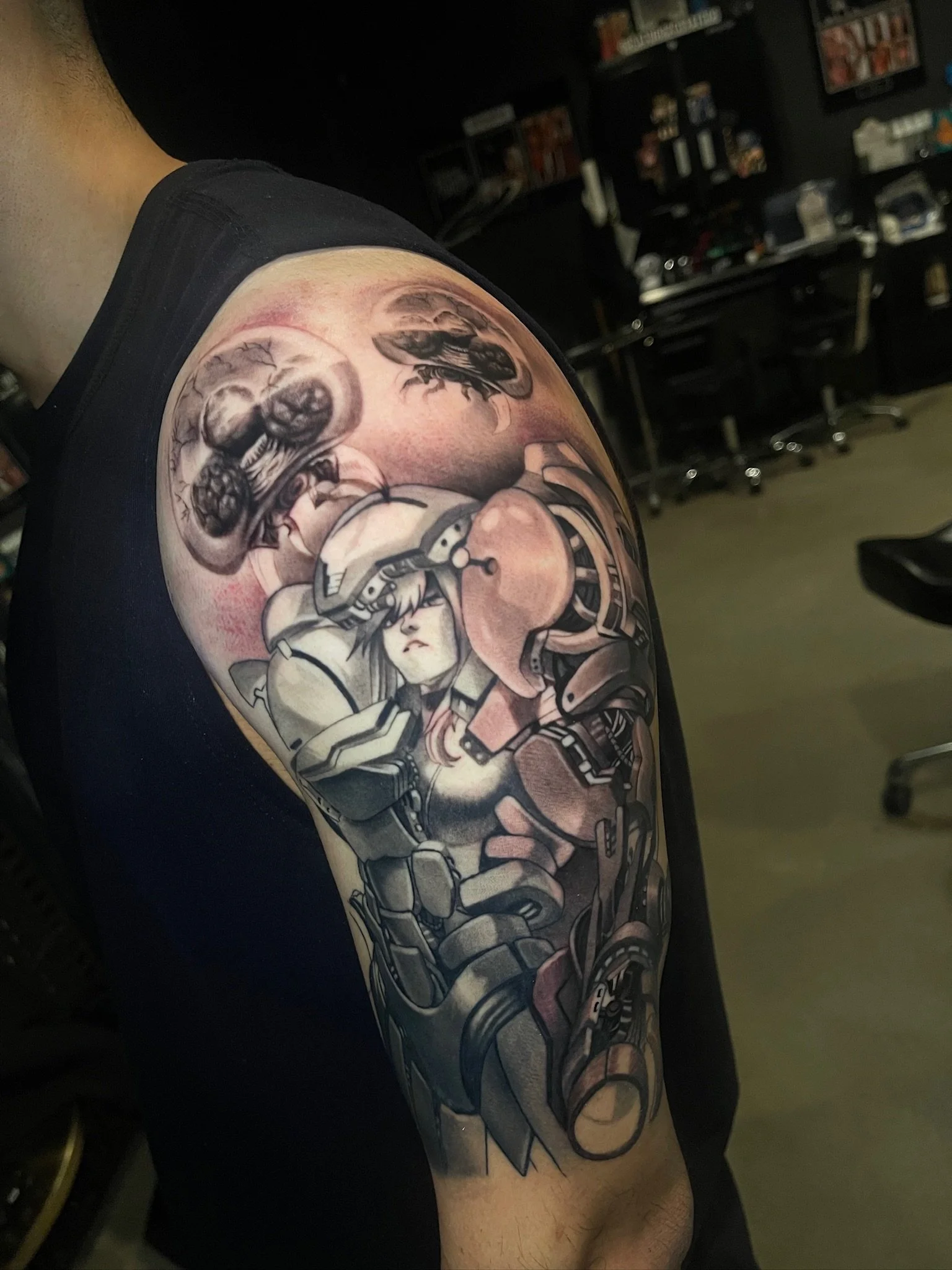 Black and gray tattoo of a female soldier in armor with a helmet, accompanied by insects and mechanical elements, on a person's upper arm.