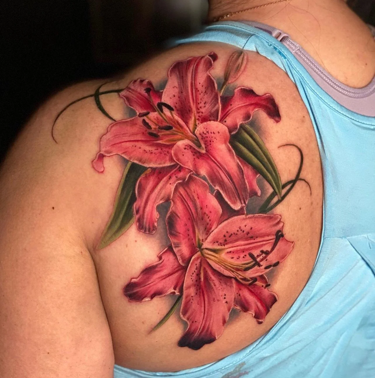 Colorful tattoo of pink lilies with green leaves on a person's shoulder