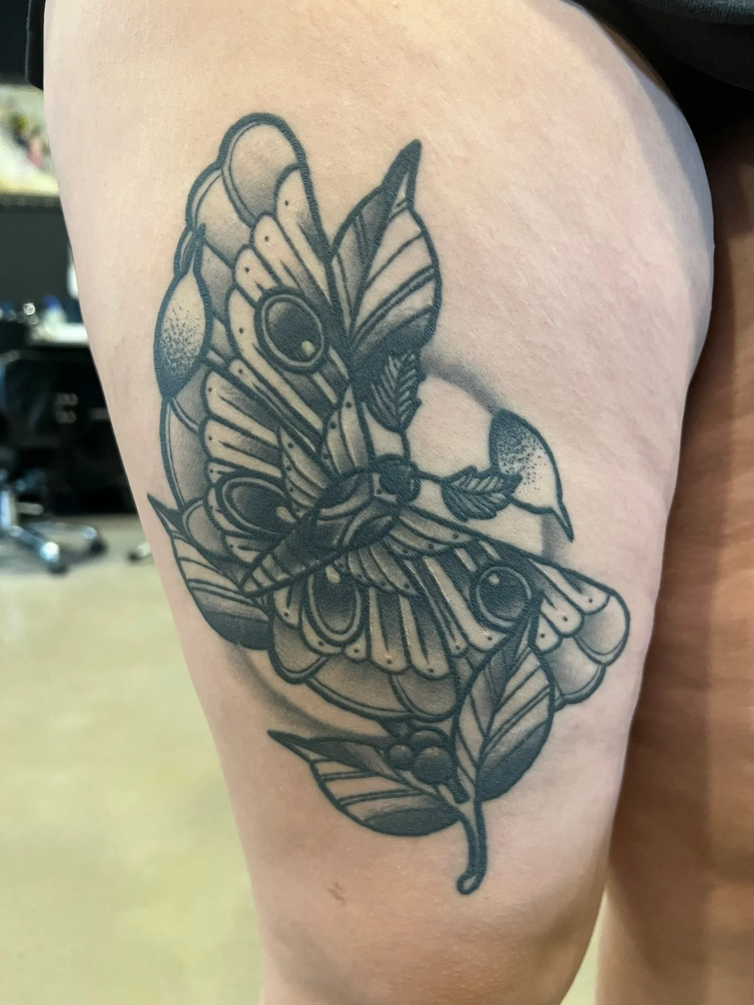 Black and gray butterfly healed tattoo on person's upper arm featuring detailed wing patterns and leaves.