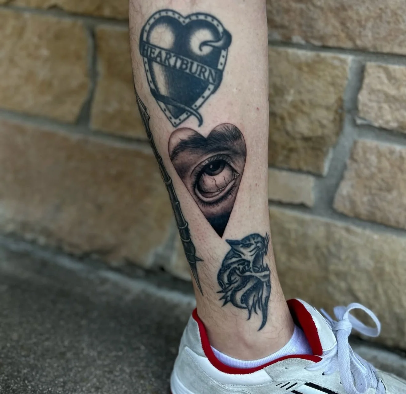 Tattoo of a Heartburn medication heart with the word "Heartburn" inside it, a realistic eye within a heart-shaped outline, and a snake wrapped around a staff.