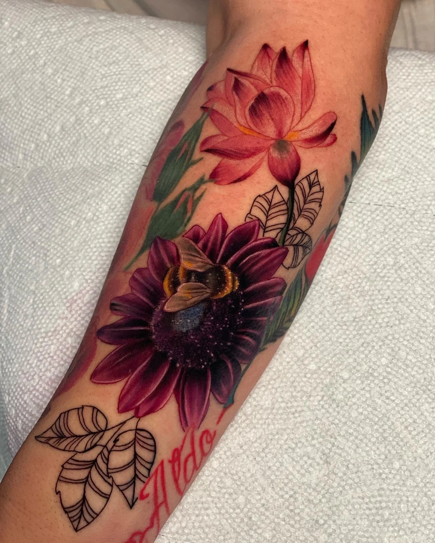 Colorful tattoo on a person's forearm featuring pink and purple flowers, a bee, and black-outlined leaves with the word 'hope' written in red.