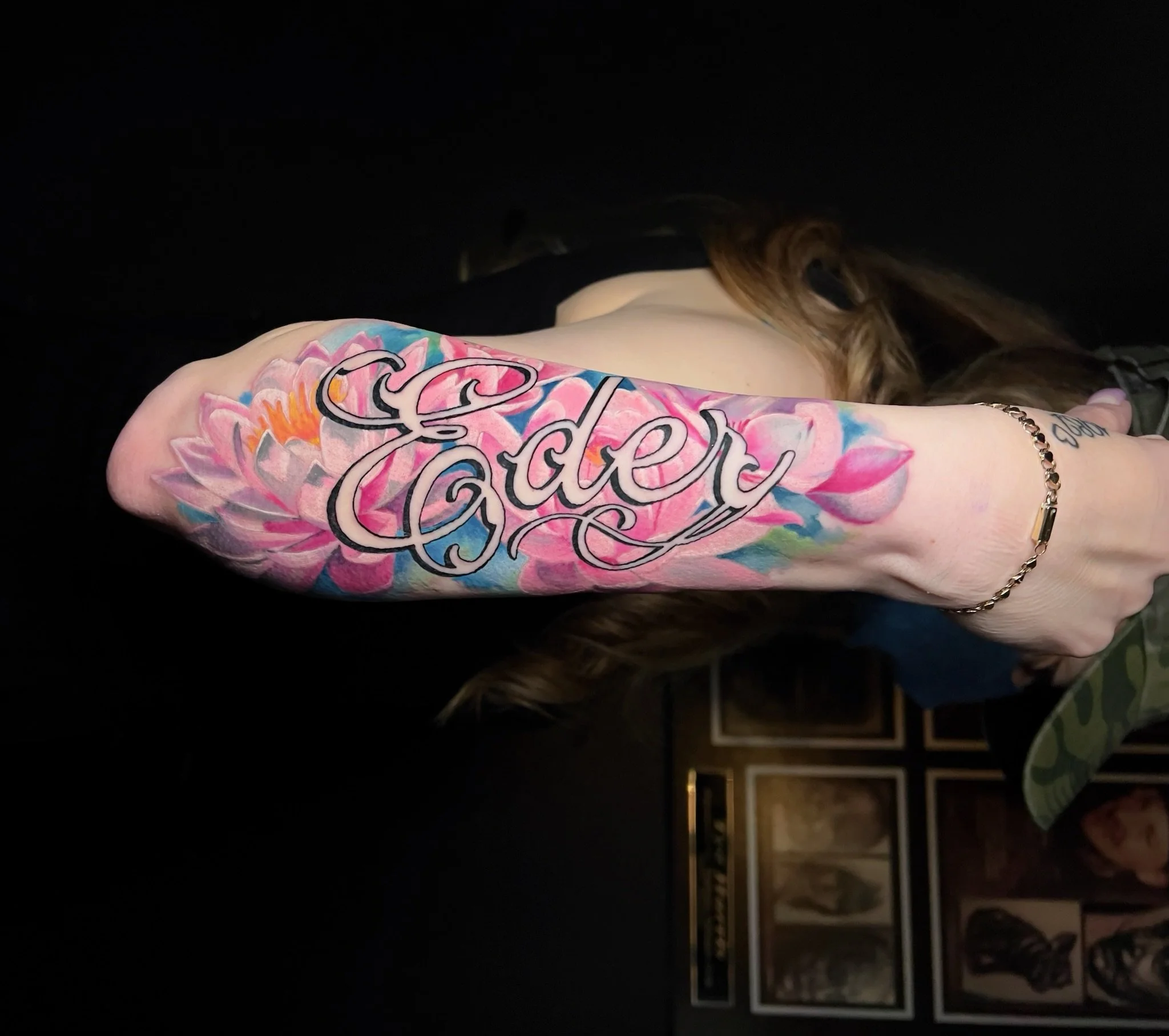 A person's arm with a colorful tattoo of pink flower petals and the name 'Carter' over the flowers.