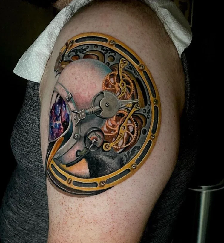 Steampunk-style tattoo of a mechanical clock on a person's upper arm, featuring gears, cogs, and intricate metalwork.