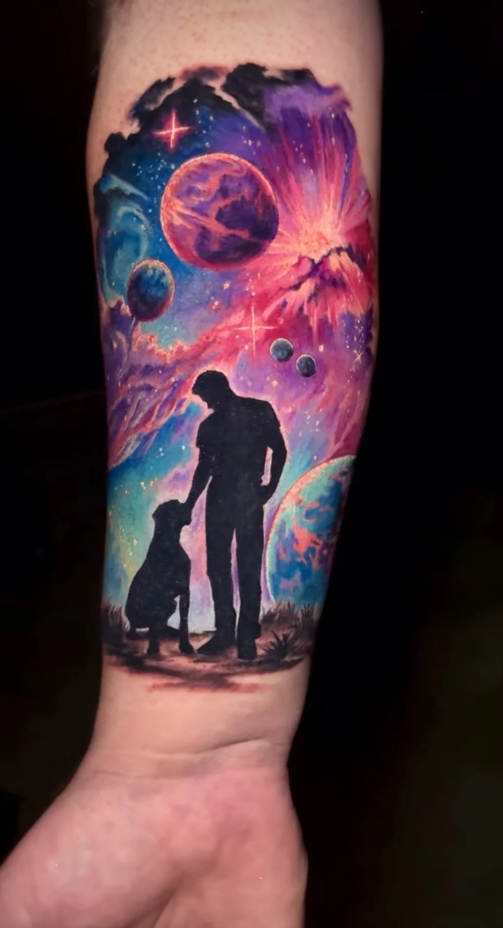 Colorful space-themed tattoo with planets, stars, and an astronaut silhouette with a dog, under a vibrant nebula and cosmic sky.