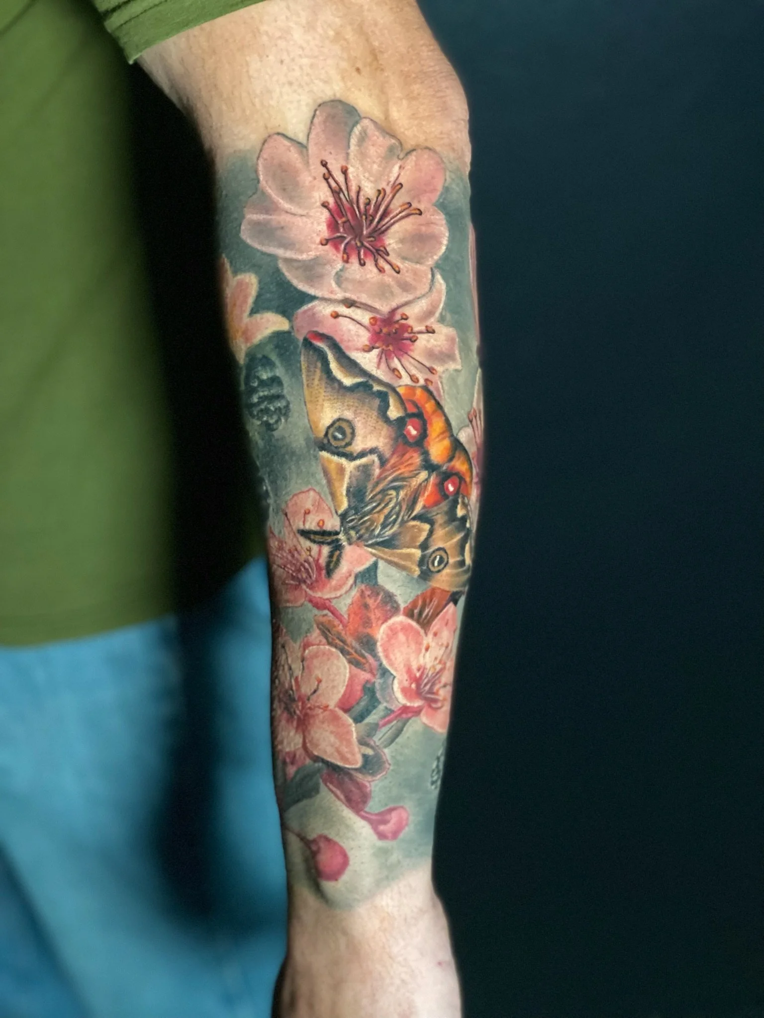 Tattoo of pink cherry blossoms and a butterfly on a person's forearm.