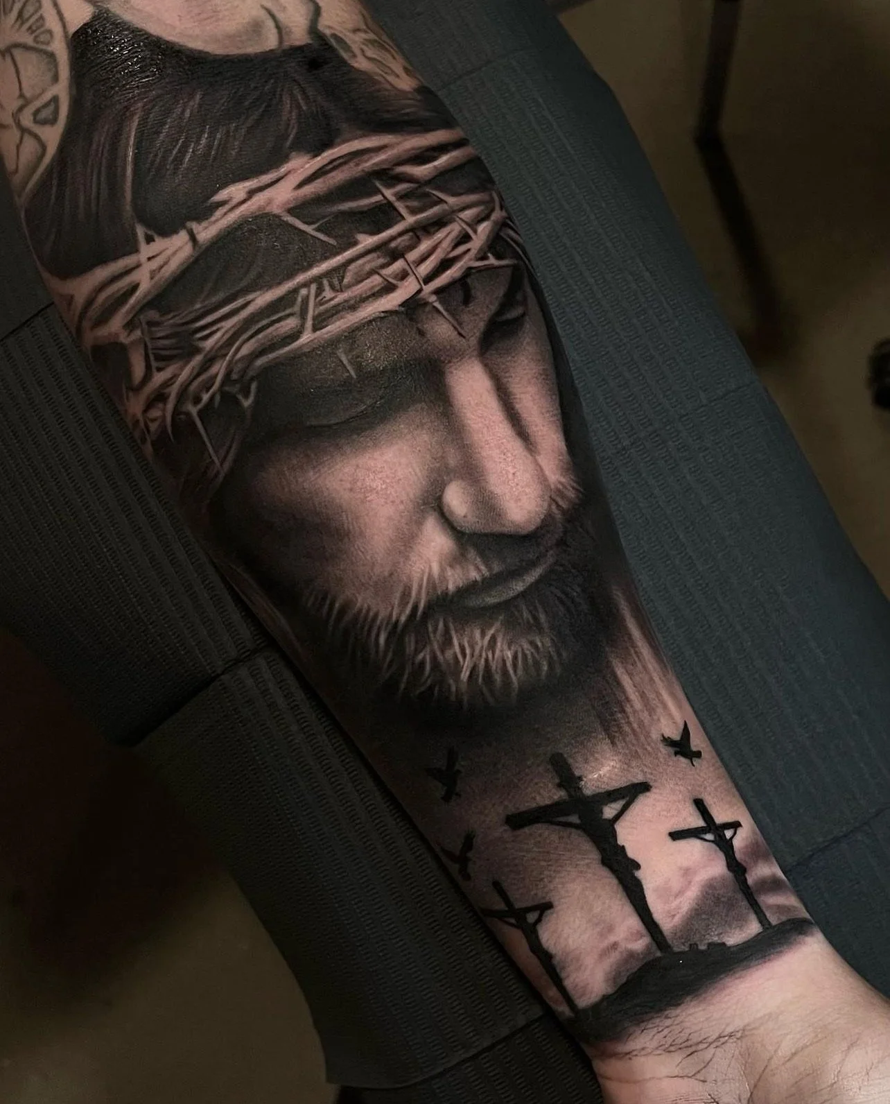Tattoo of Jesus Christ's face with a crown of thorns and five crosses below his chin, covering most of a person's arm.