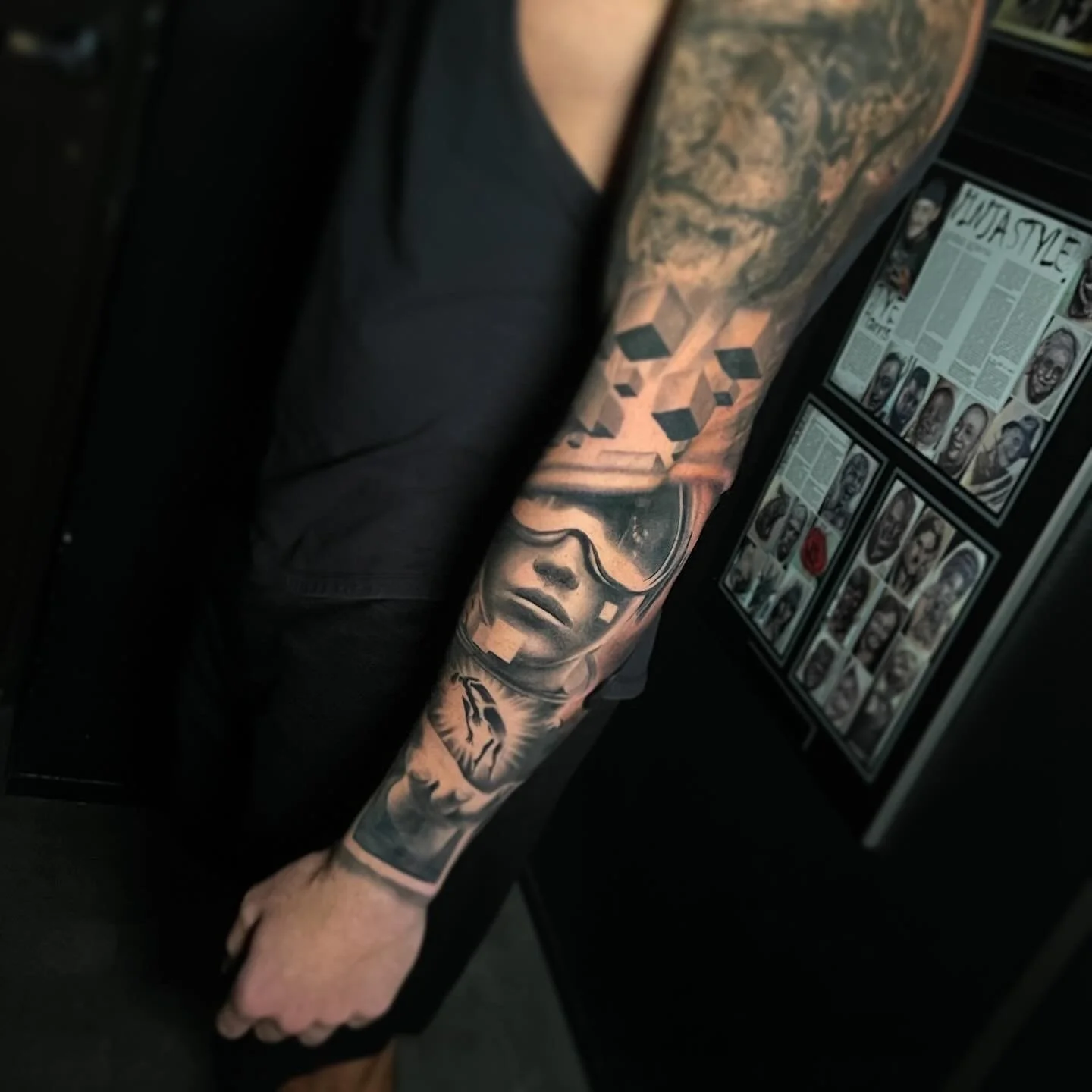 Tattooed arm with geometric shapes, a woman's face wearing goggles, and other designs.