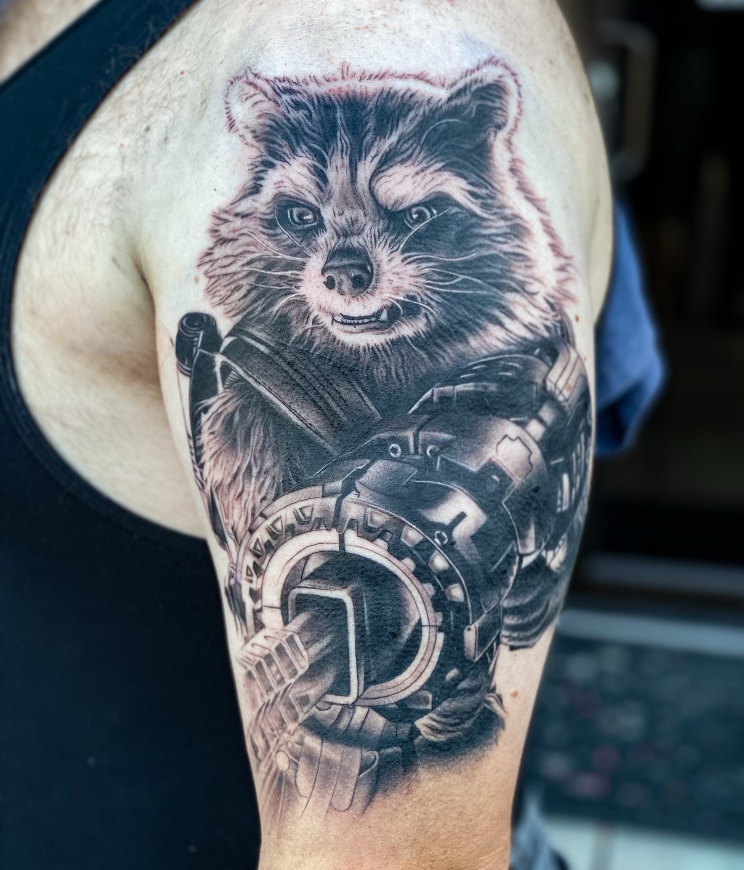 Tattoo of a raccoon with a mischievous expression, holding a futuristic weapon.
