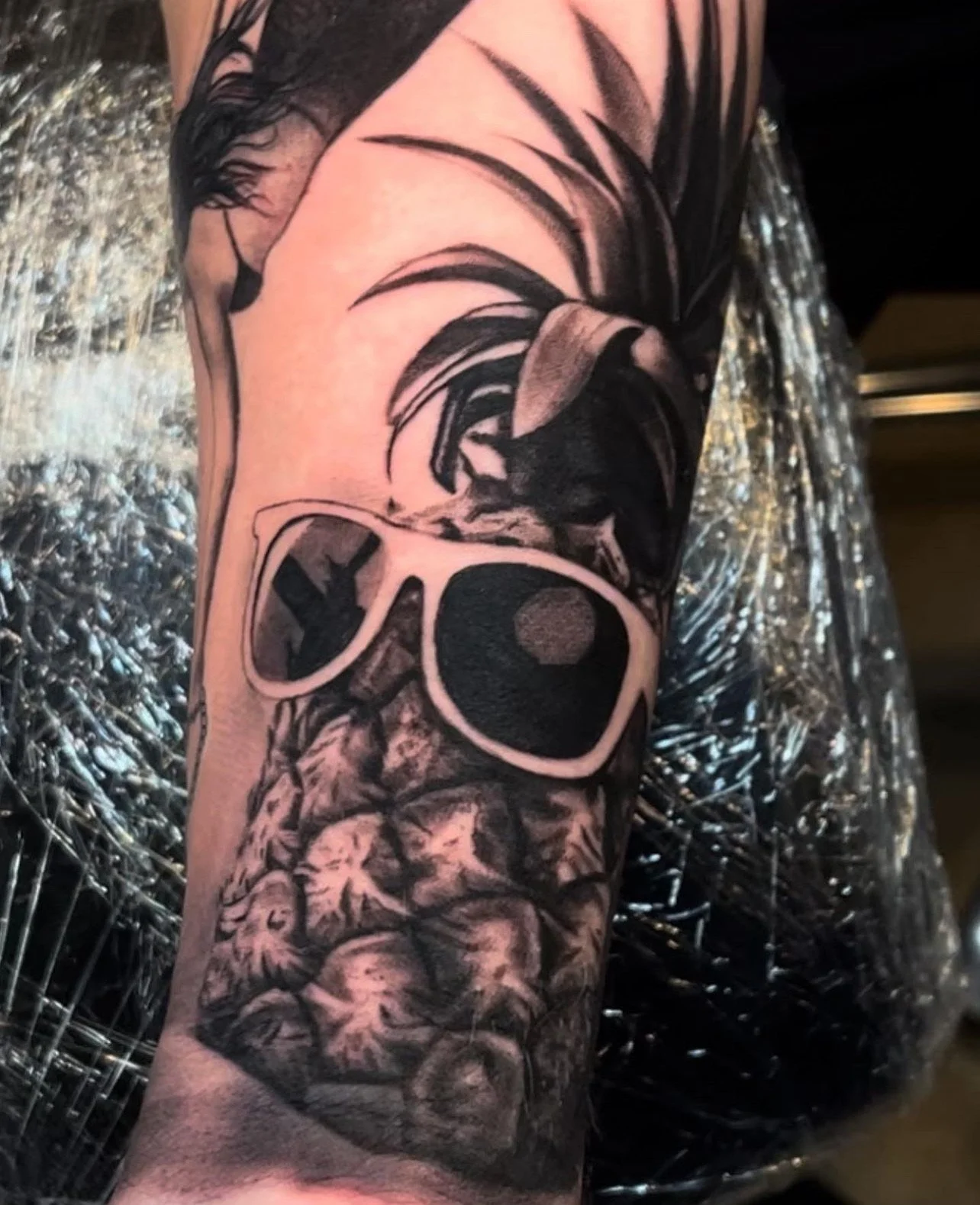 Black and gray tattoo with a skull wearing sunglasses, surrounded by leaves and abstract designs.