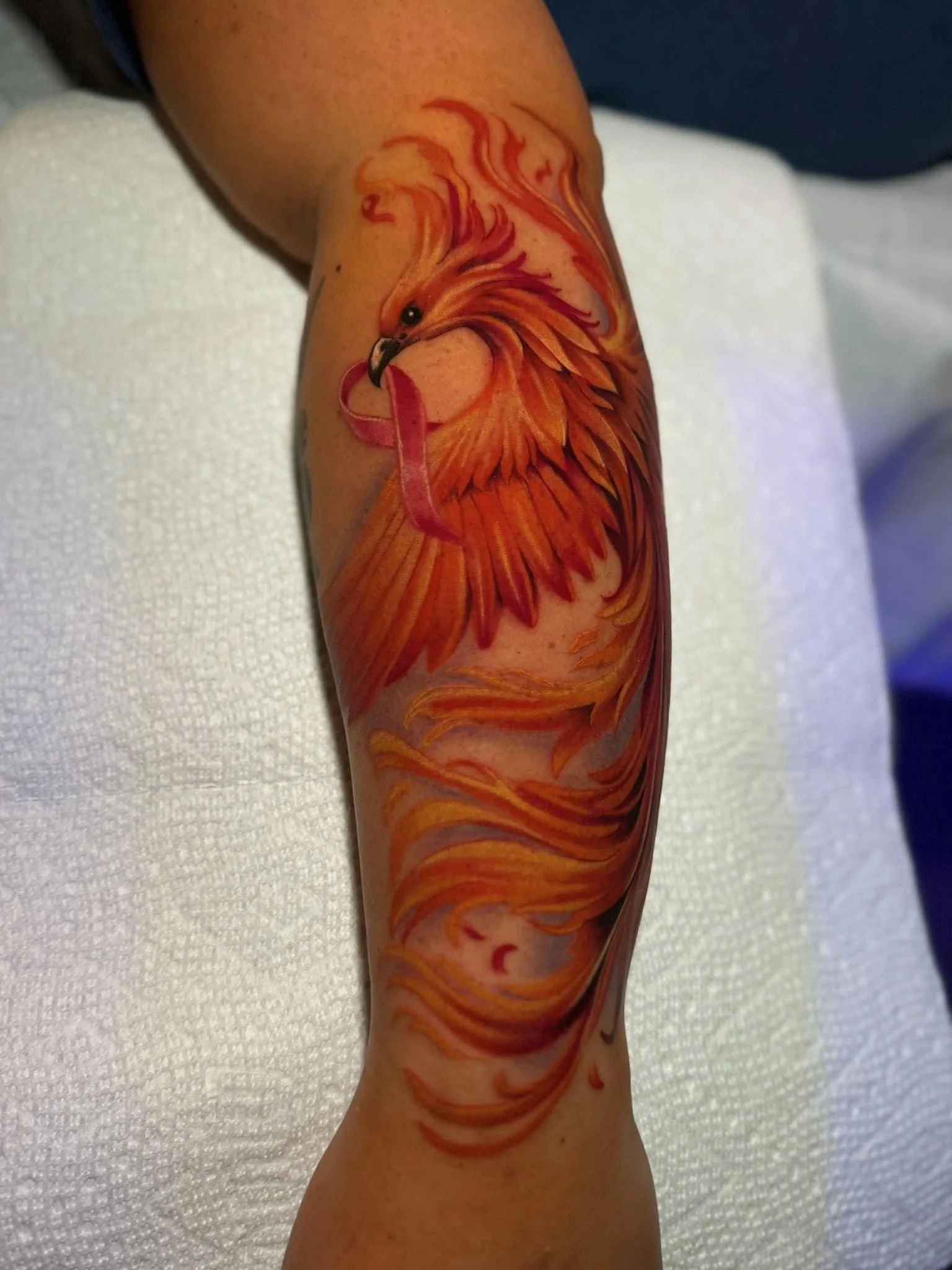 Colorful tattoo of a phoenix with orange, red, and yellow flames on a person's arm.