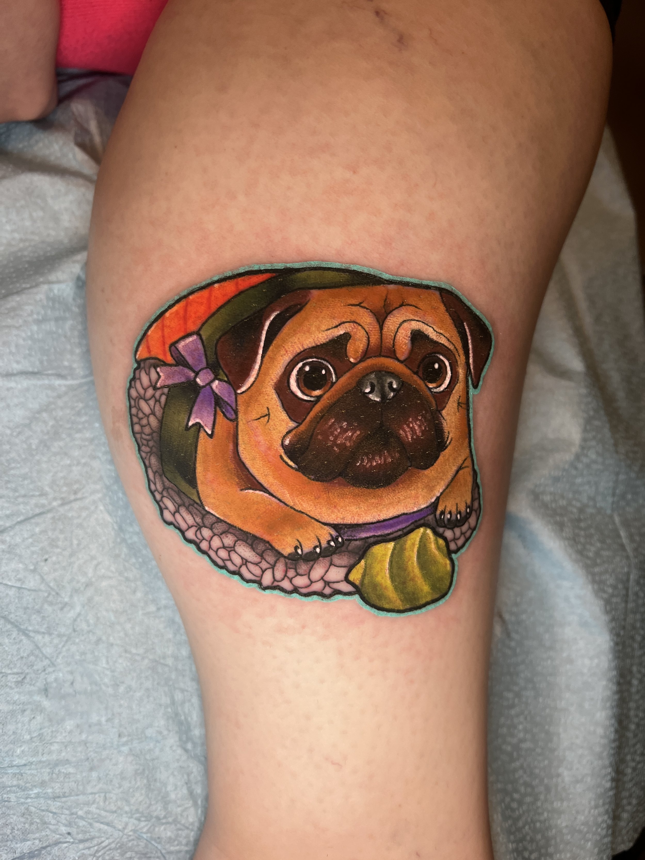 Tattoo of a cute dog wearing a colorful hat, on a person's thigh.