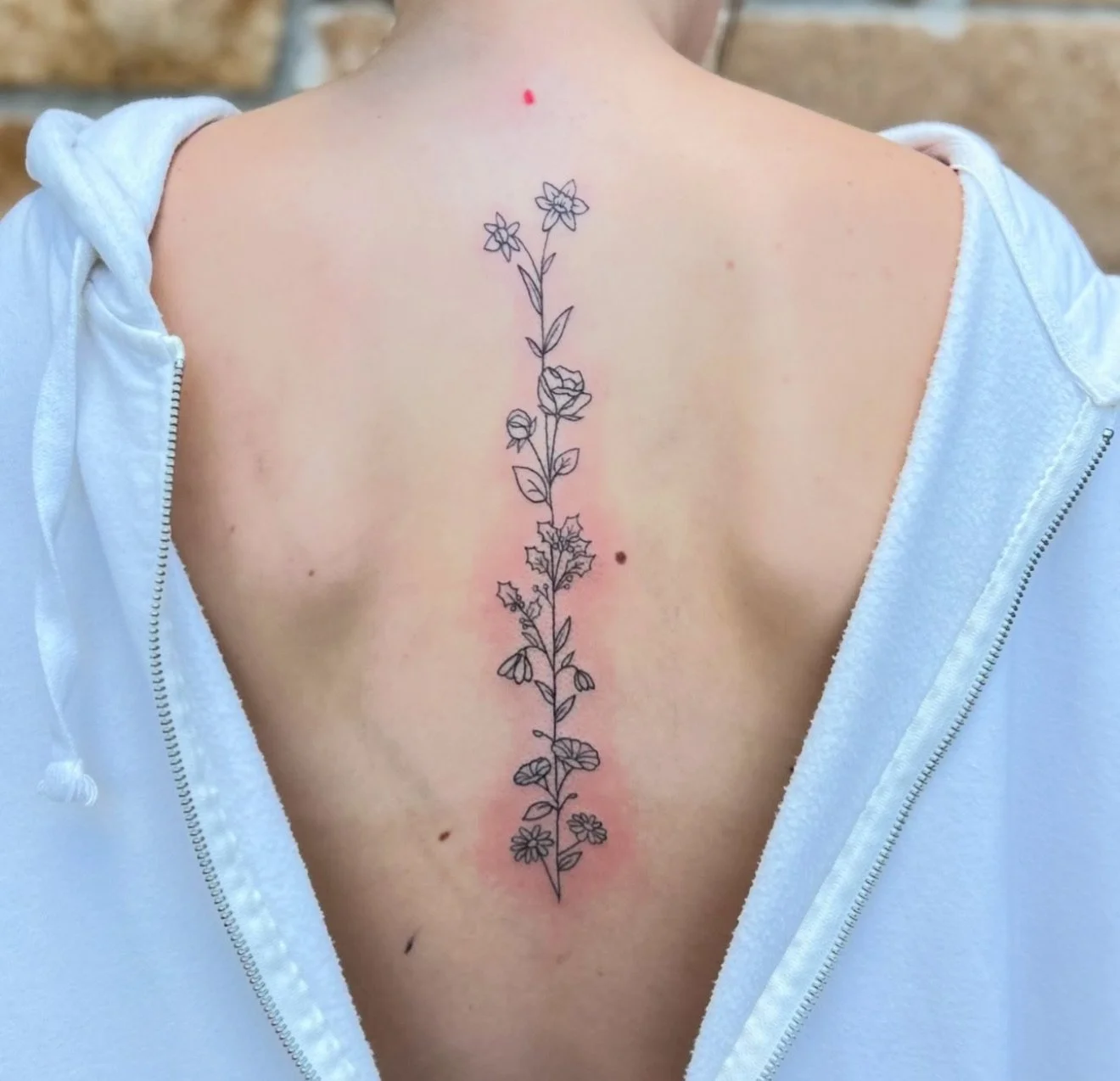 A person's back with a temporary tattoo of a simple black outline floral design running vertically down the spine, with some redness around the tattoo.