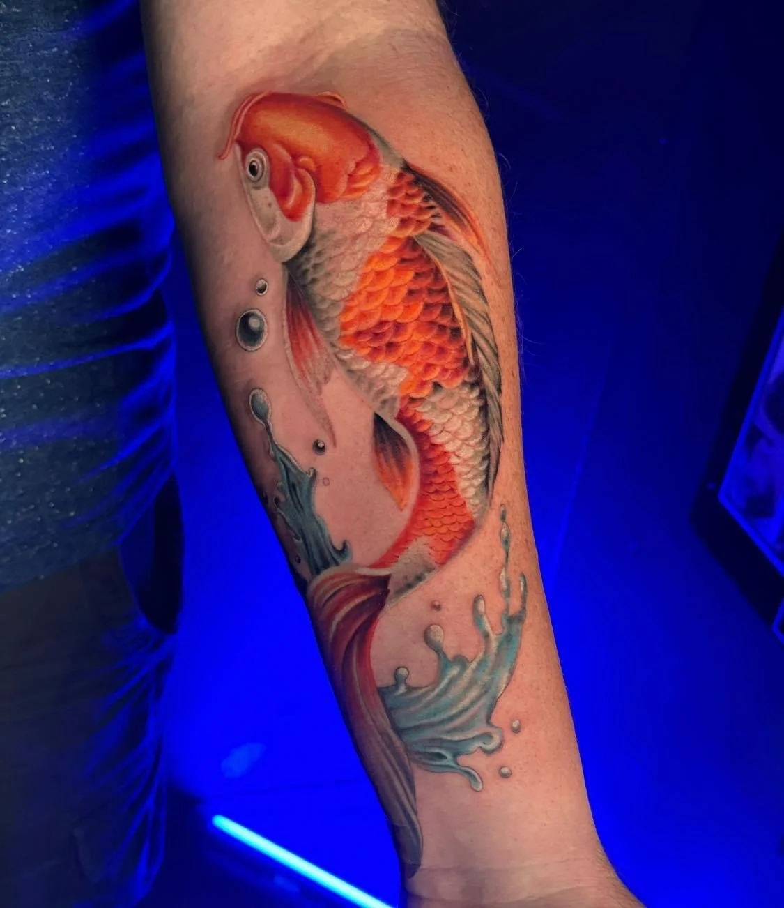 Colorful tattoo of a goldfish swimming with water splashes on a person's forearm.