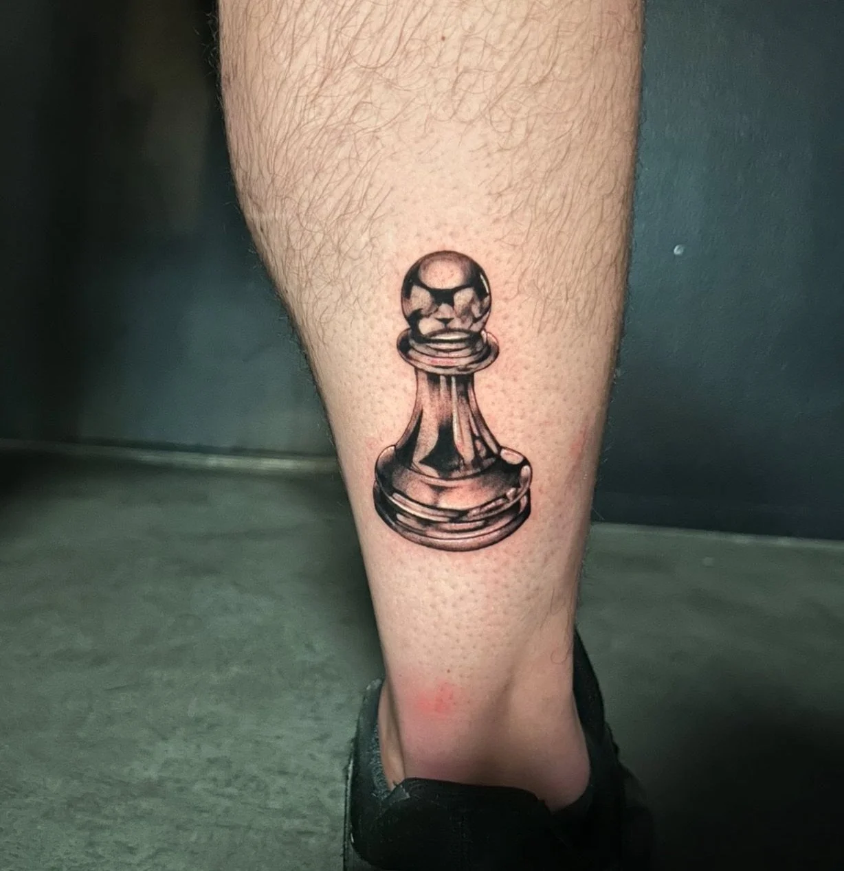 Tattoo of a chess pawn on a person's lower leg.