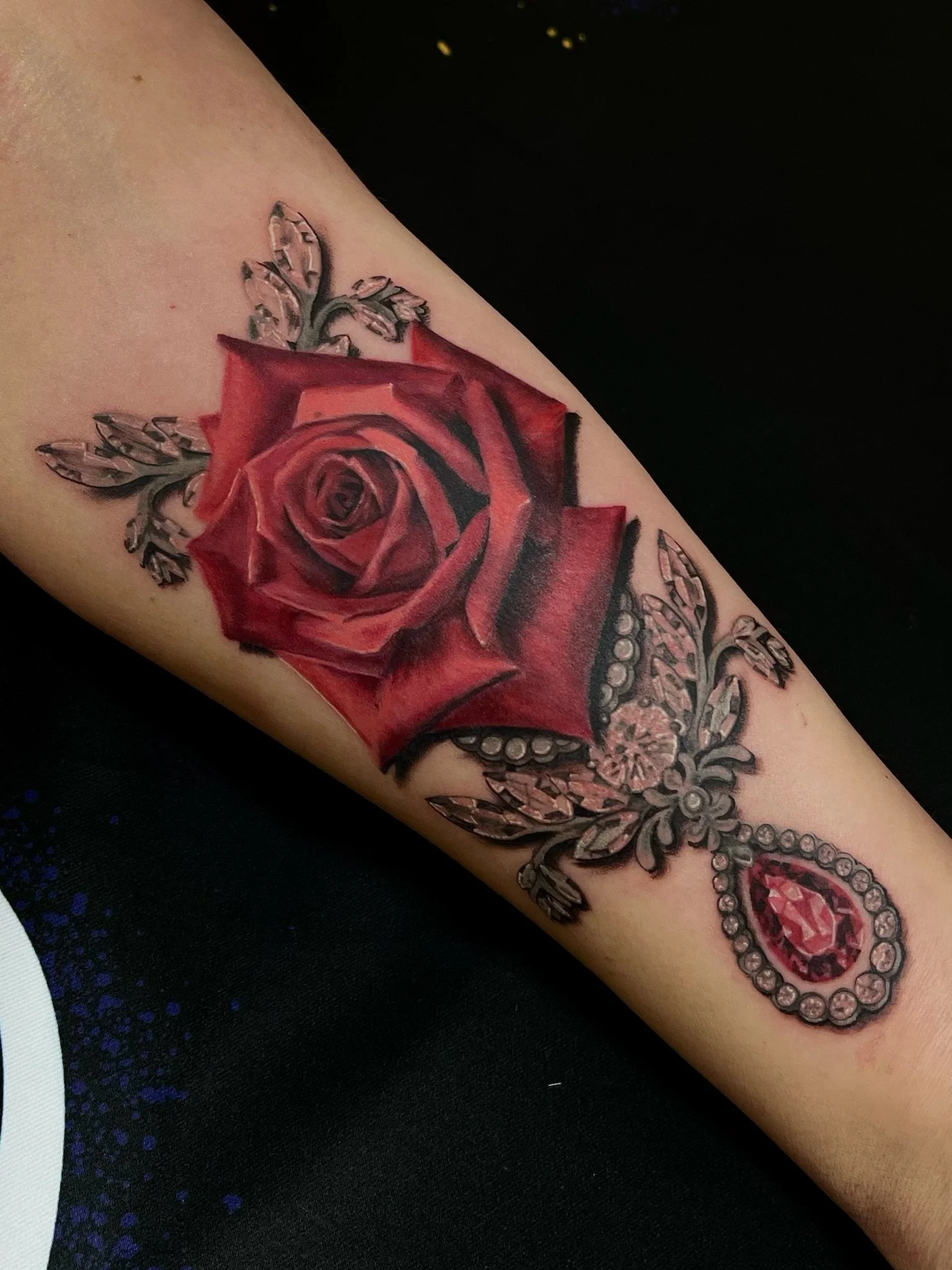 Colorful tattoo of a red rose with leaves and decorative elements on a person's arm.