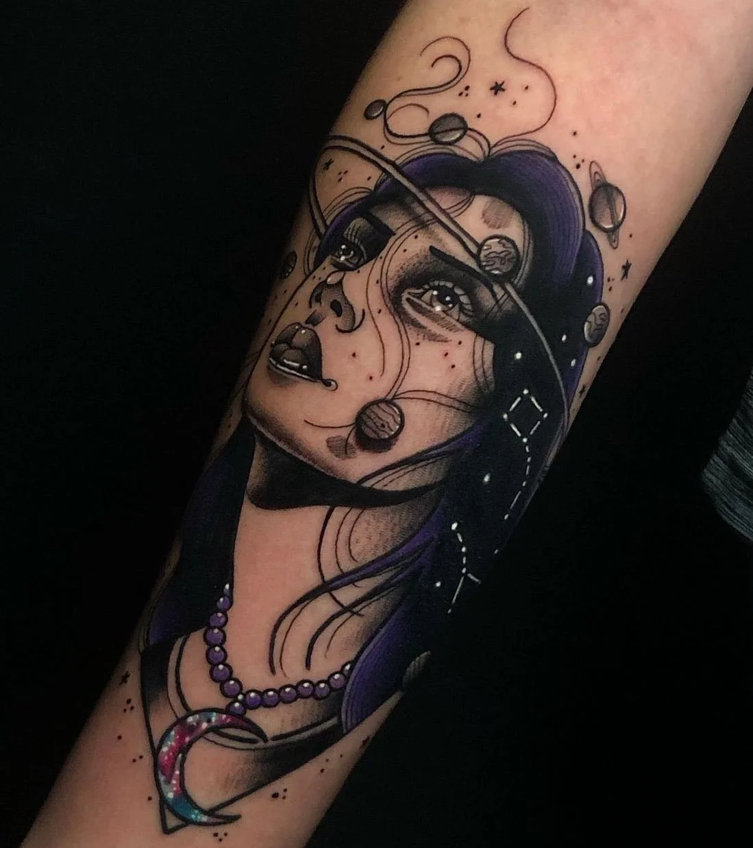 Tattoo of a woman's face with cosmic and space elements, including planets and stars, with purple hair and a pearl necklace.