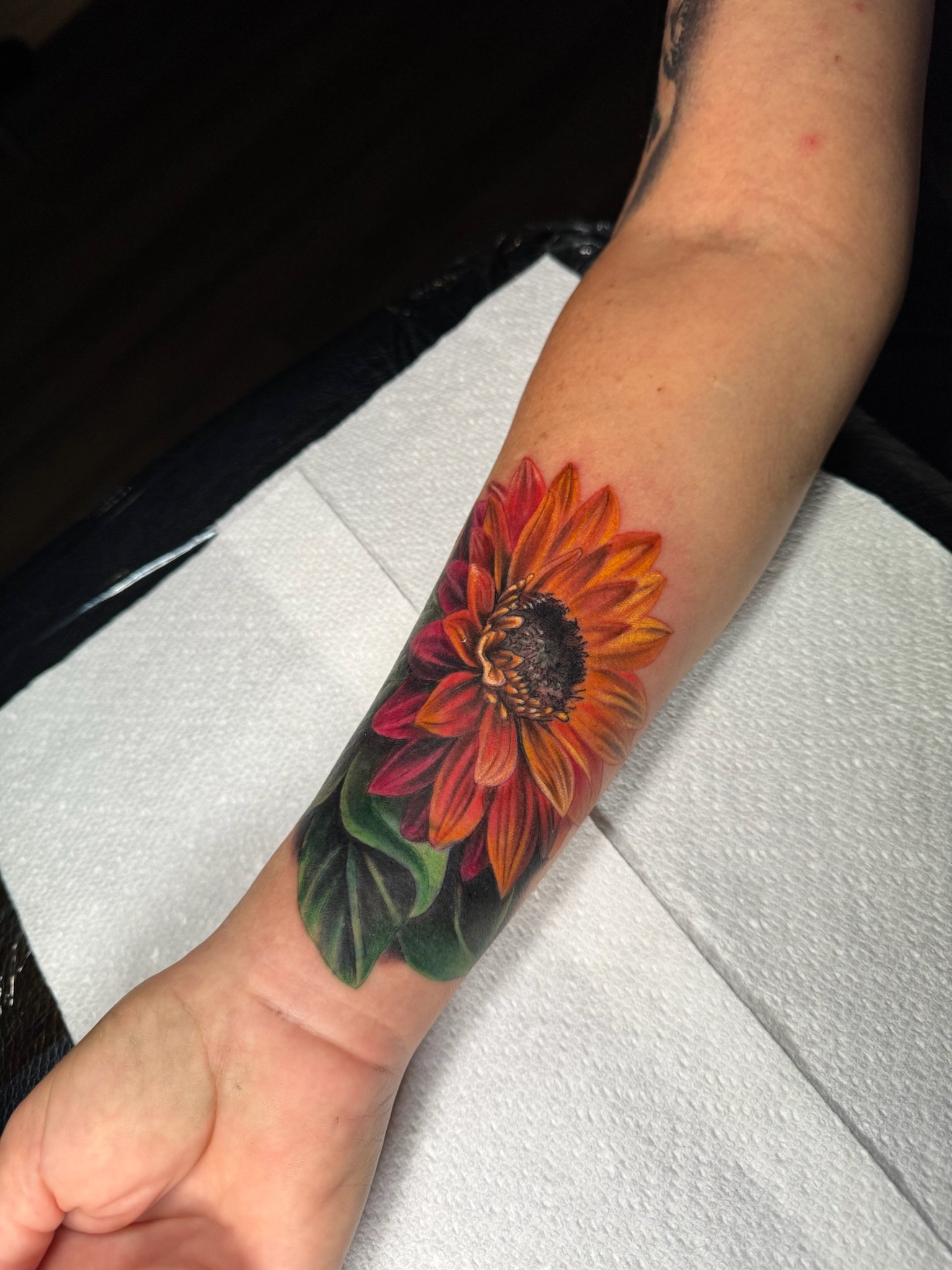 Tattoo of a sunflower on a person's forearm.