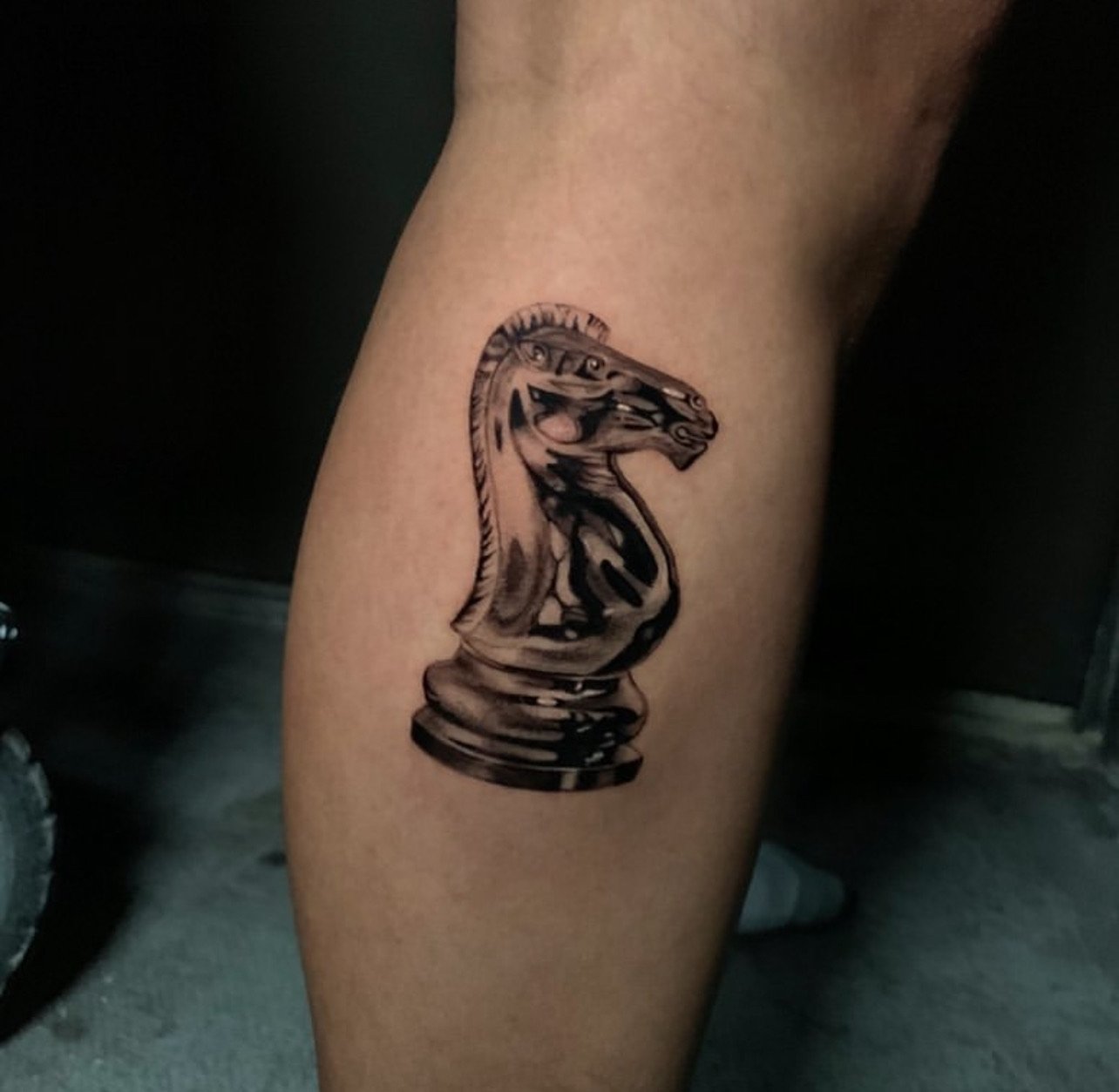 Tattoo of a chess knight piece on a person's leg.