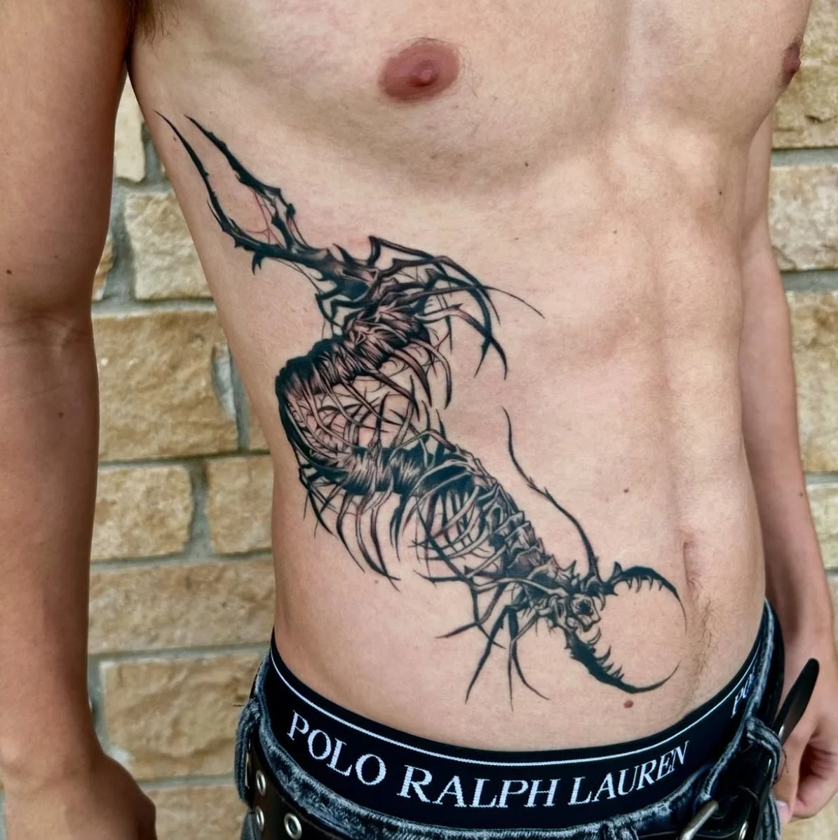 Tattoo of a black and gray, detailed, stylized scorpion on a person's side torso.