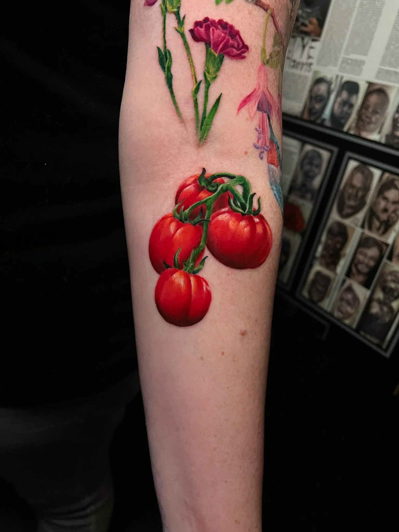 Colorful tattoo of a bunch of red tomatoes on the vine and purple flowers on a person's arm.