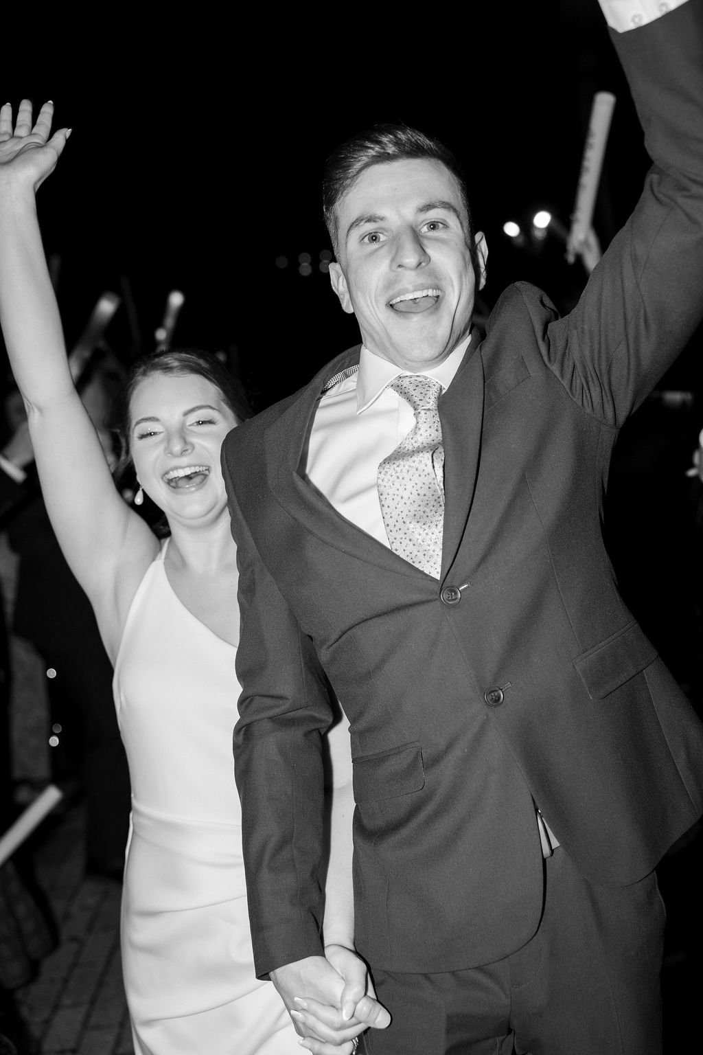 A joyful man and woman celebrating together, holding hands and smiling at night.