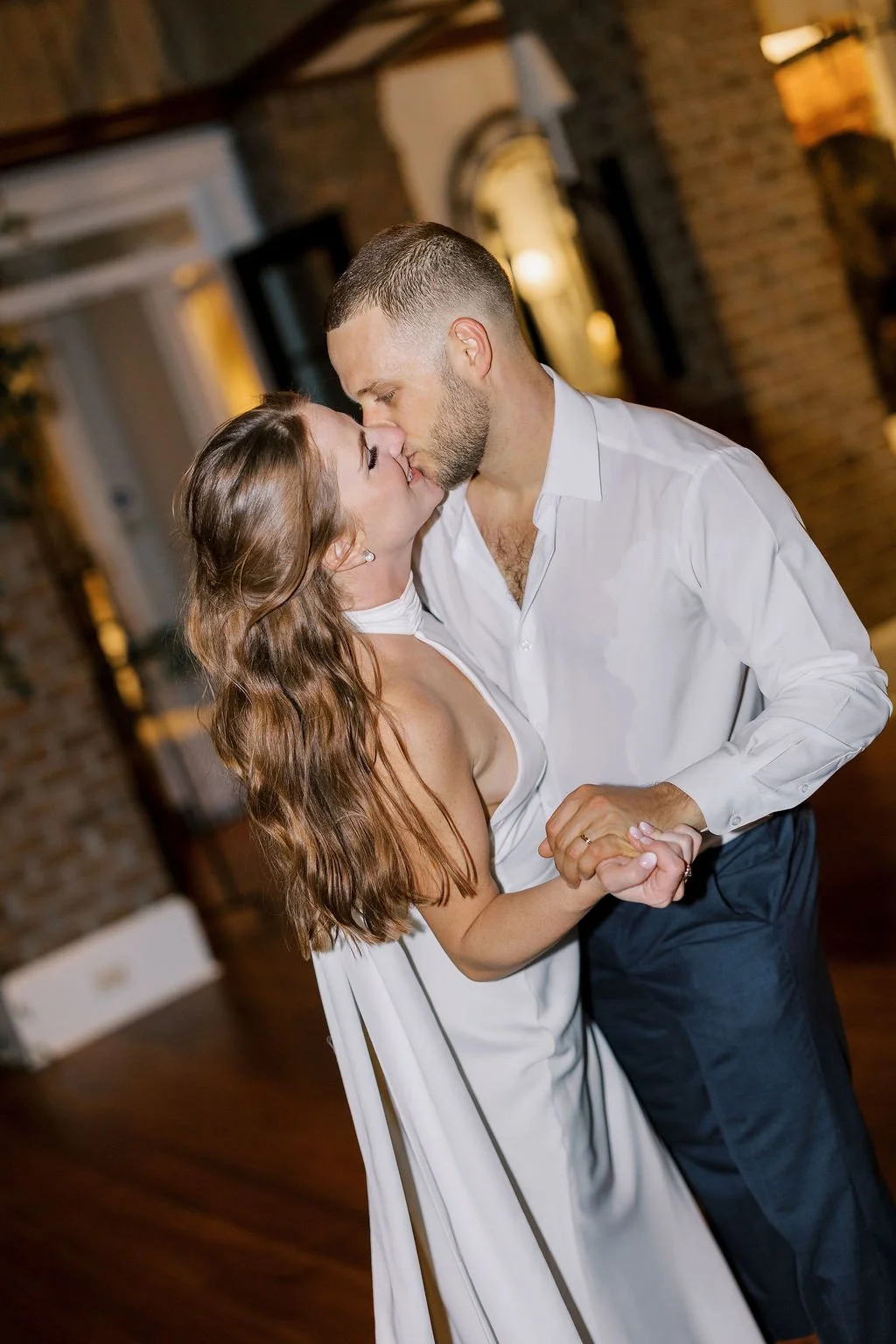 A couple dancing closely, about to kiss, in an indoor venue with warm lighting and brick walls.