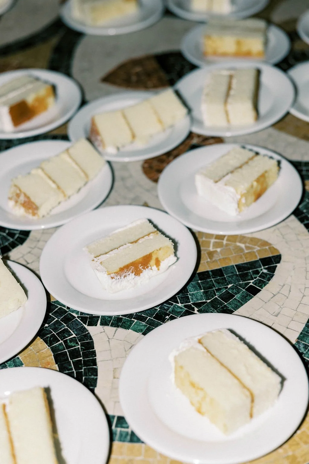 Multiple plates with slices of layered cake on a mosaic table.