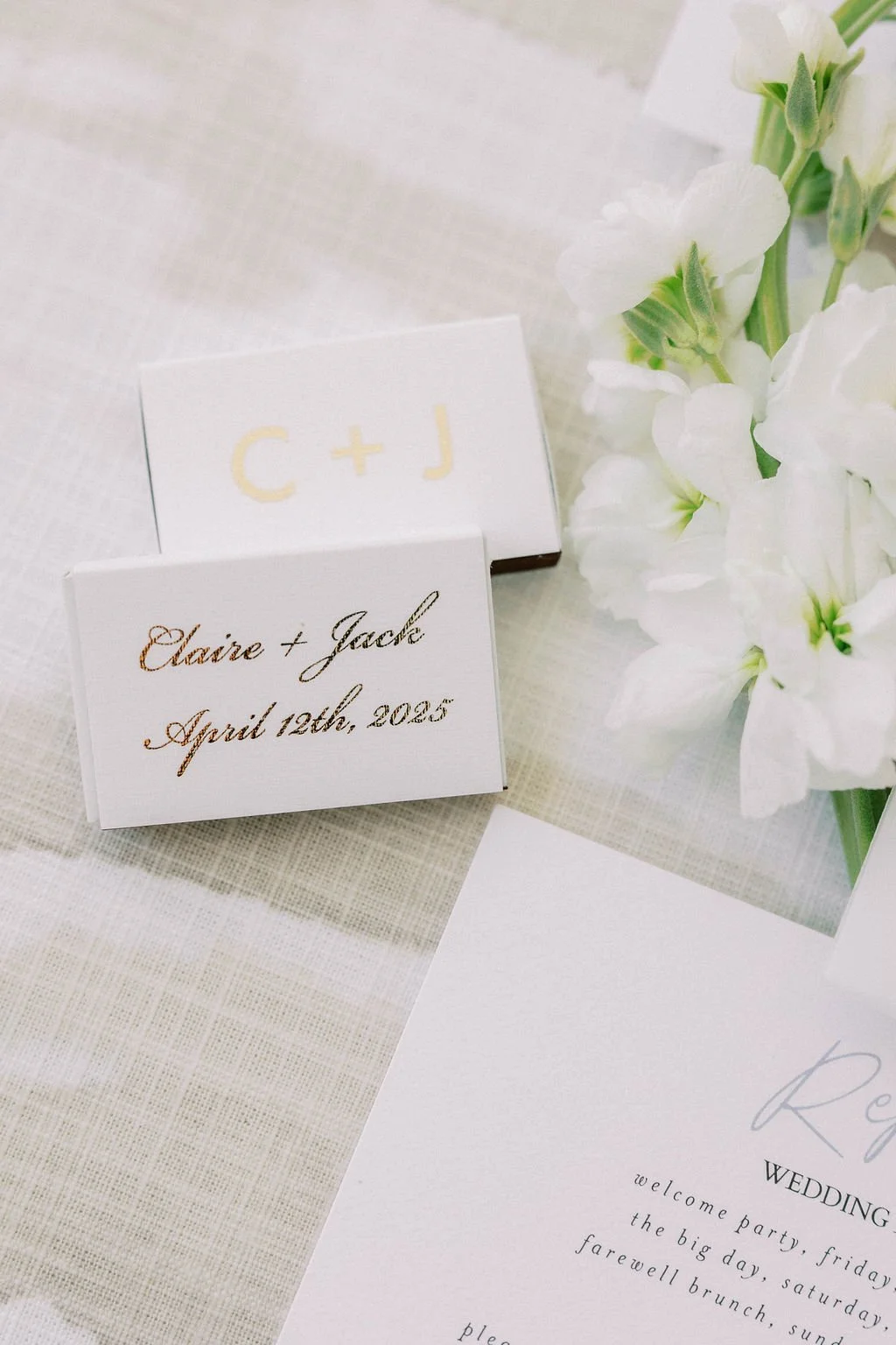 Wedding place cards with the names Claire and Jack and the date April 12th, 2023, next to white flowers on a table.