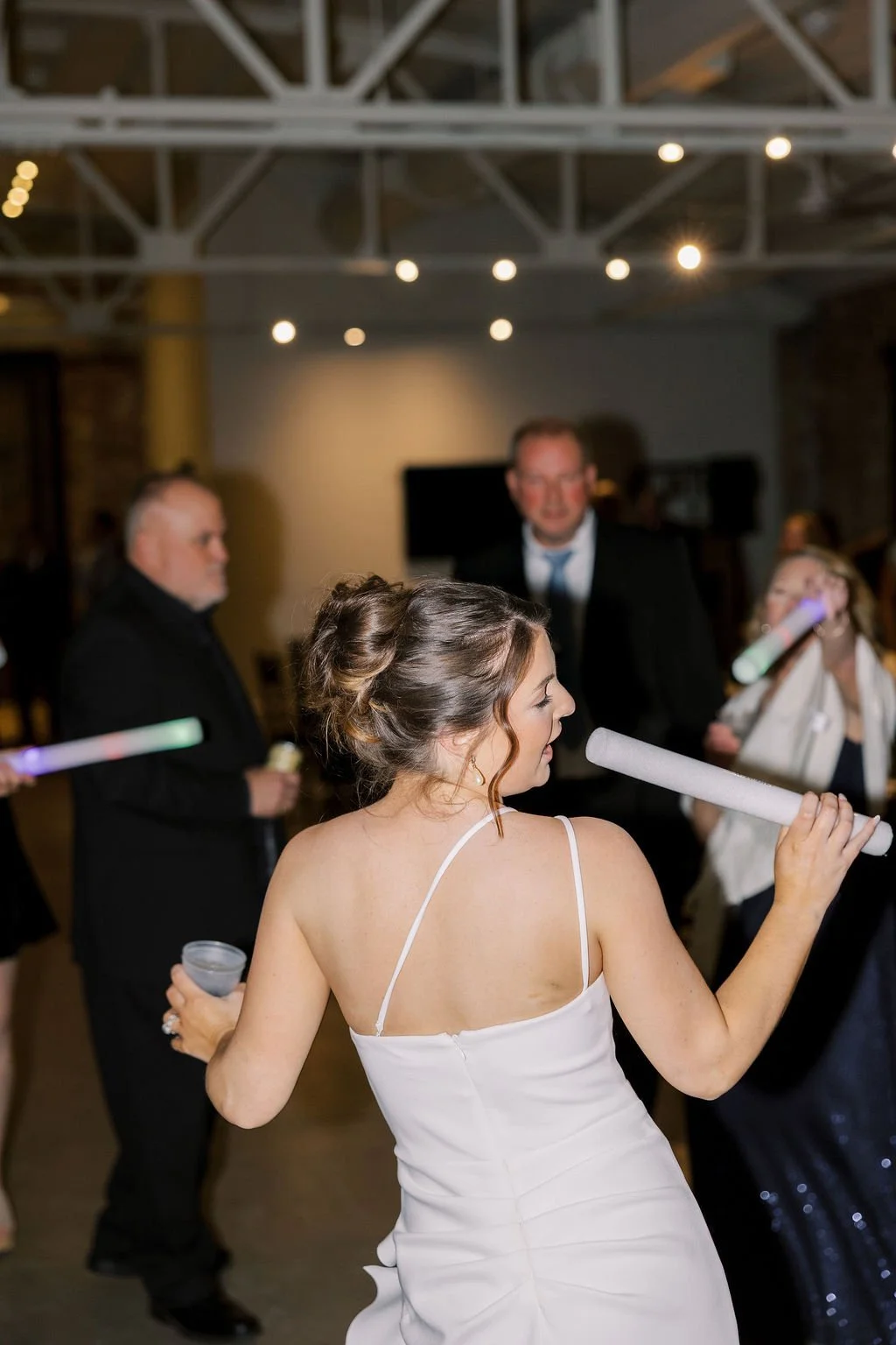 Woman in white dress dancing with glow sticks at a party.