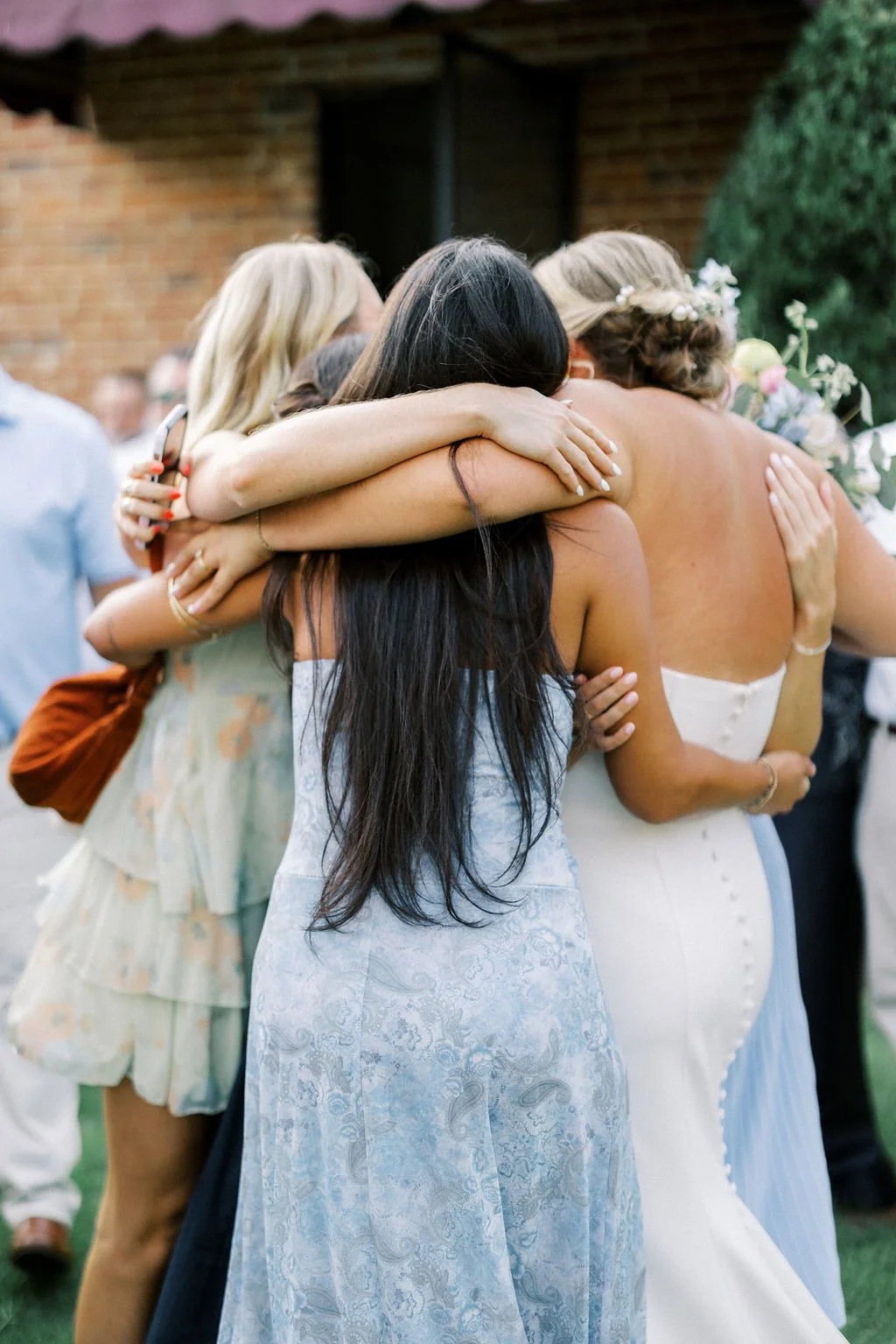 Group of women hugging at a wedding or celebration outdoors.