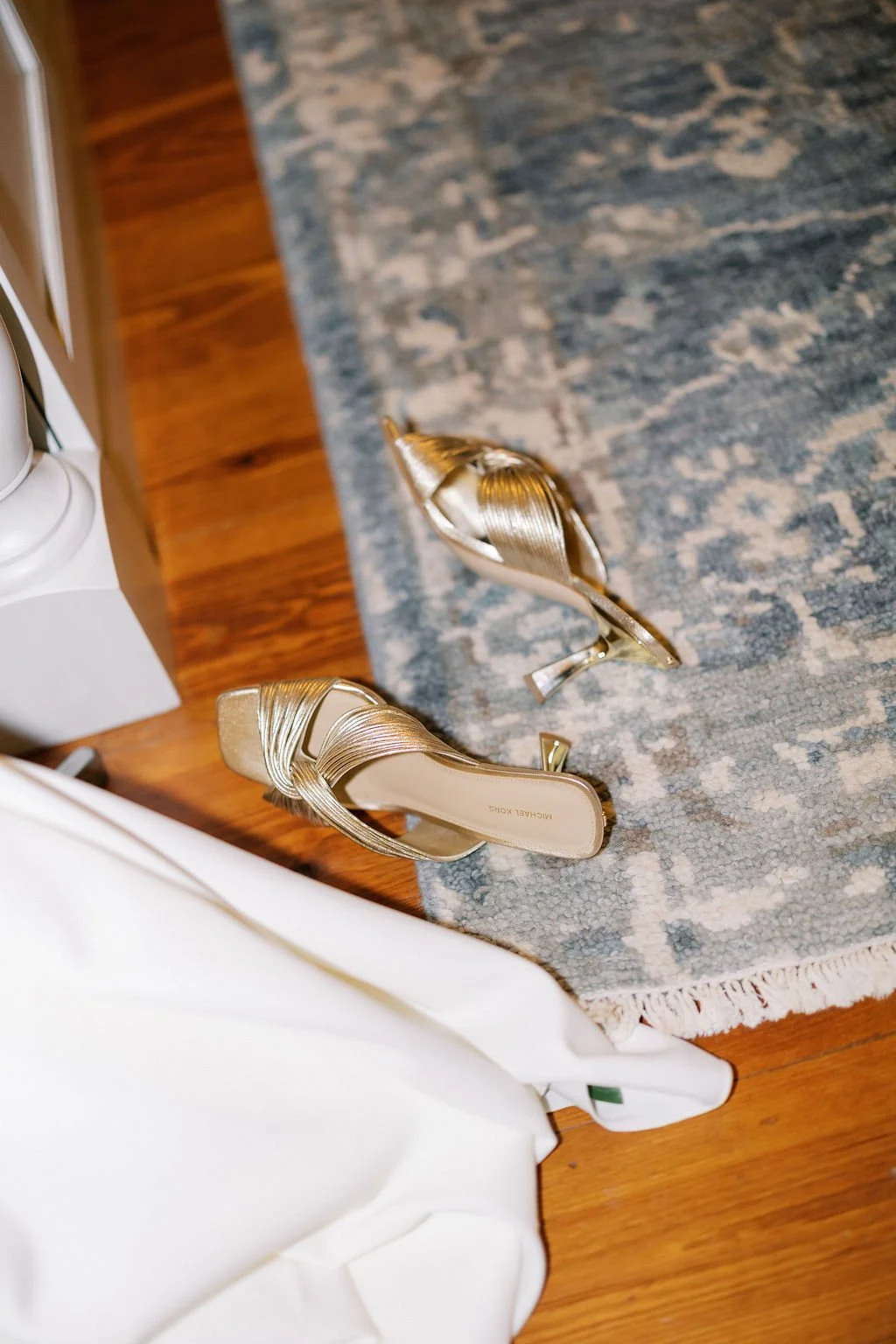 A pair of gold high-heeled sandals with crisscross straps resting on a blue and beige patterned rug.