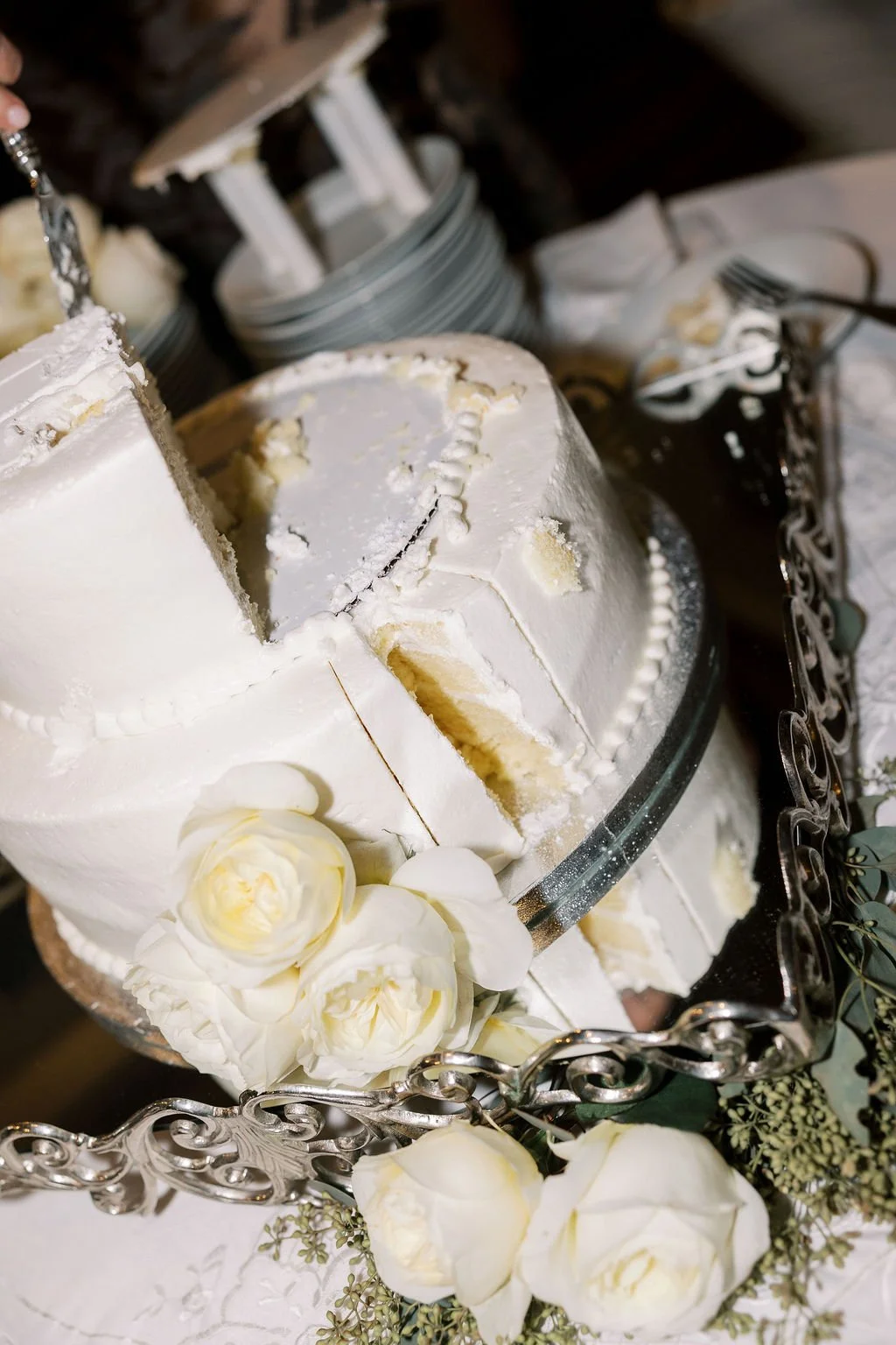 A partially sliced white wedding cake decorated with white roses and floral accents, placed on a decorative silver tray.