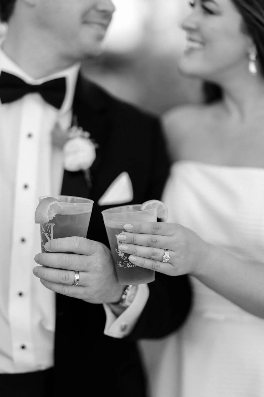 A couple dressed in formal wedding attire holding drinks with lemon slices, smiling at each other.
