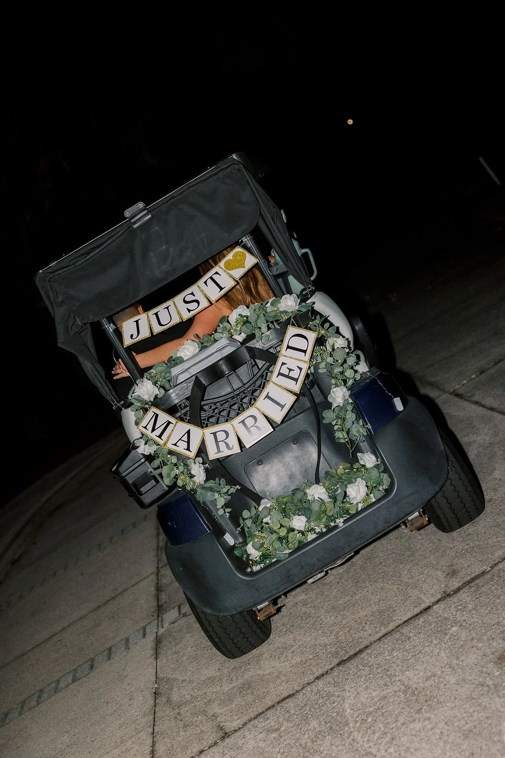 Golf cart decorated with white flowers and green foliage, with a banner reading "JUST MARRIED."