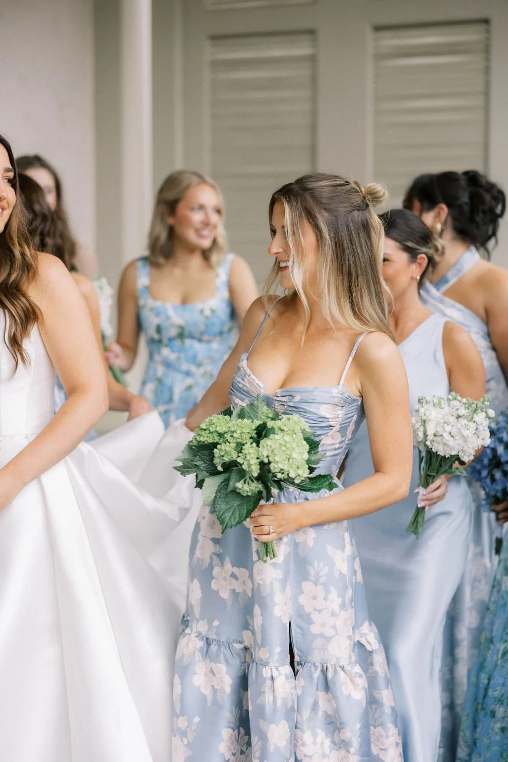 A group of women in blue and white dresses holding bouquets of flowers, smiling and talking at a wedding reception.