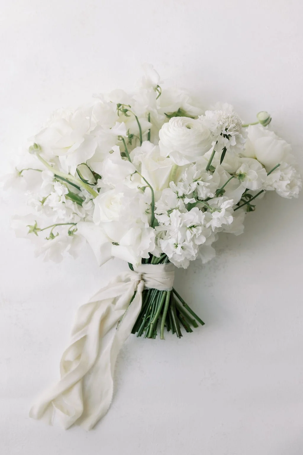 A bouquet of white flowers tied with a white ribbon against a white background.