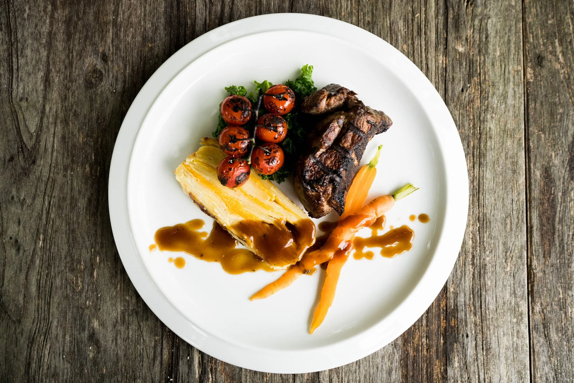 A crisp white plate with rump of lamb, dauphinoise potatoes and cherry vine tomatoes.