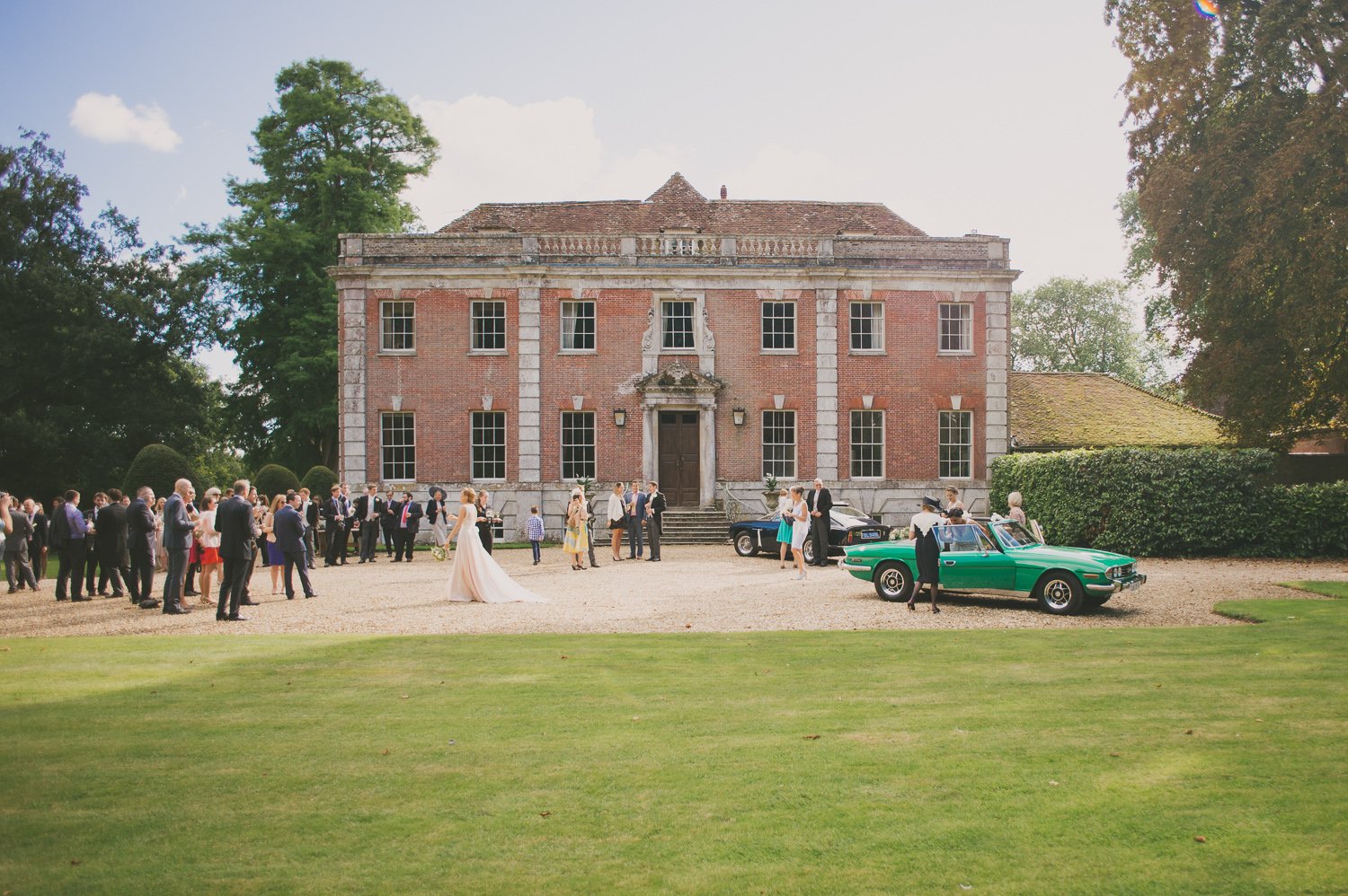 Wedding gathering outside Deans Court in Dorset with vintage cars and guests in formal attire