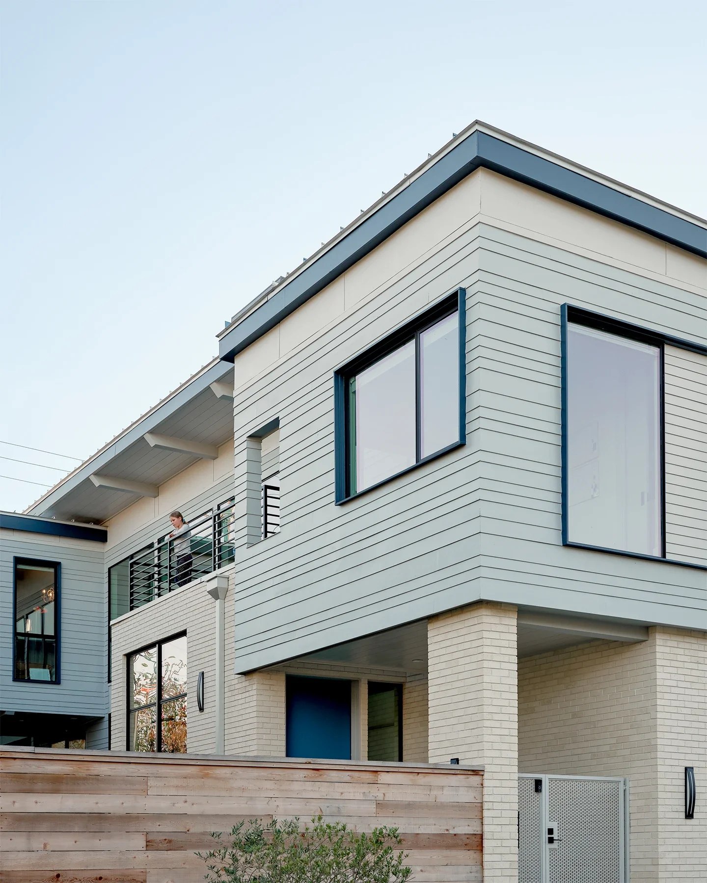 Modern multi-story residential building with large windows, some open, and a person on the balcony.