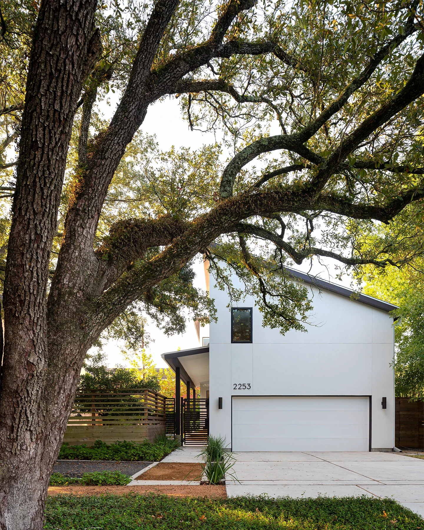 Modern white house with a two-car garage, surrounded by trees and greenery.
