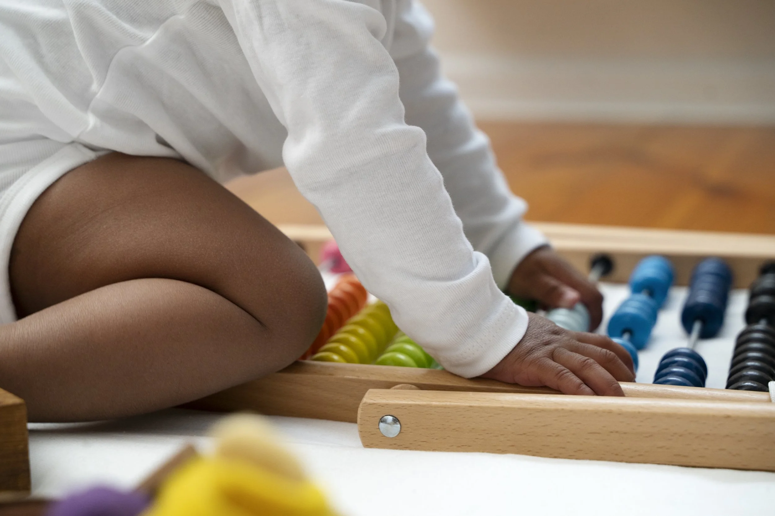 A child kneeling on the floor using a colorful abacus with beads in orange, yellow, green, blue, and black.