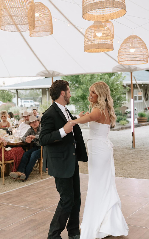 A couple dancing under hanging wicker pendant lights at an outdoor wedding reception.