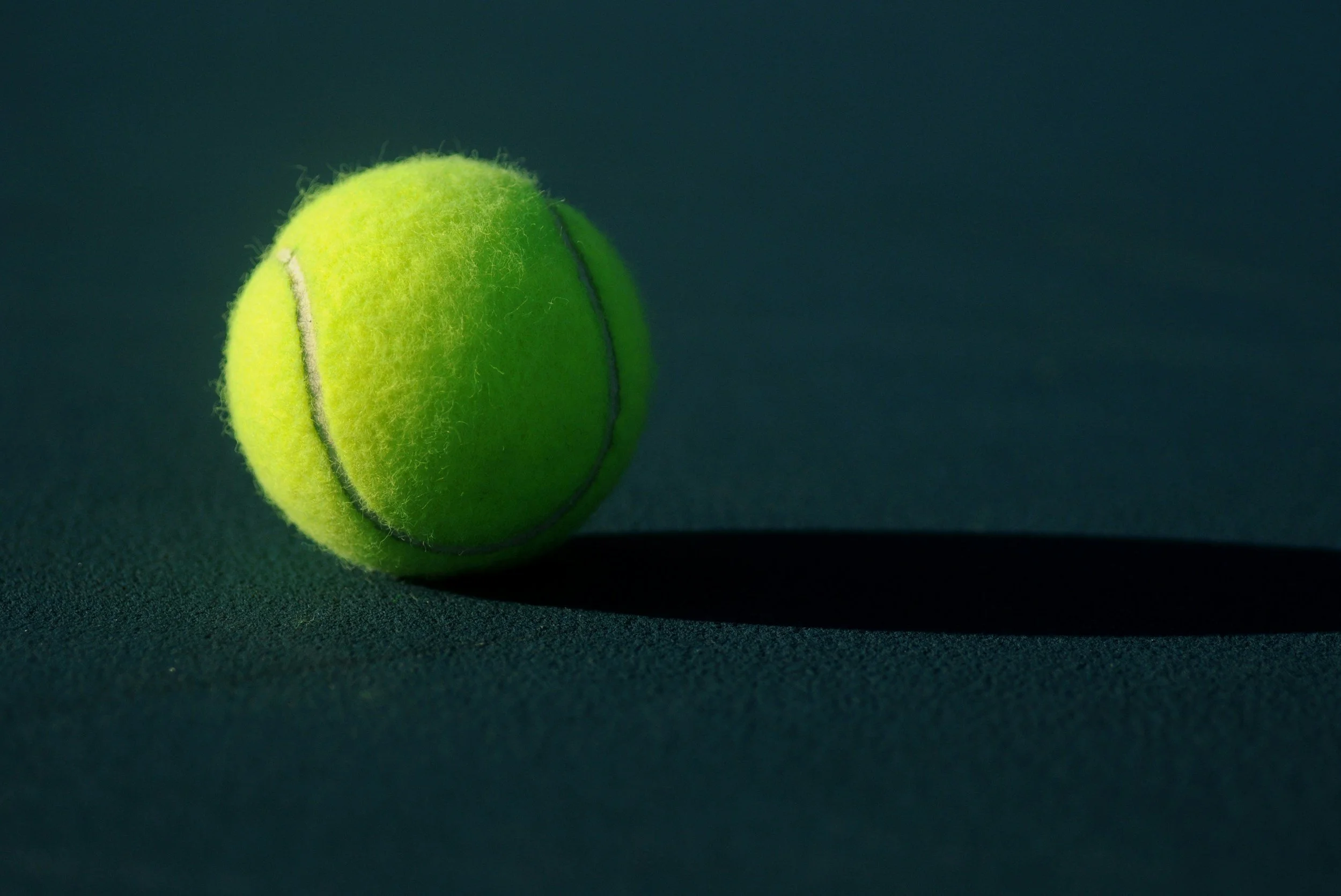 Close-up of a green tennis ball on a dark surface with shadow.