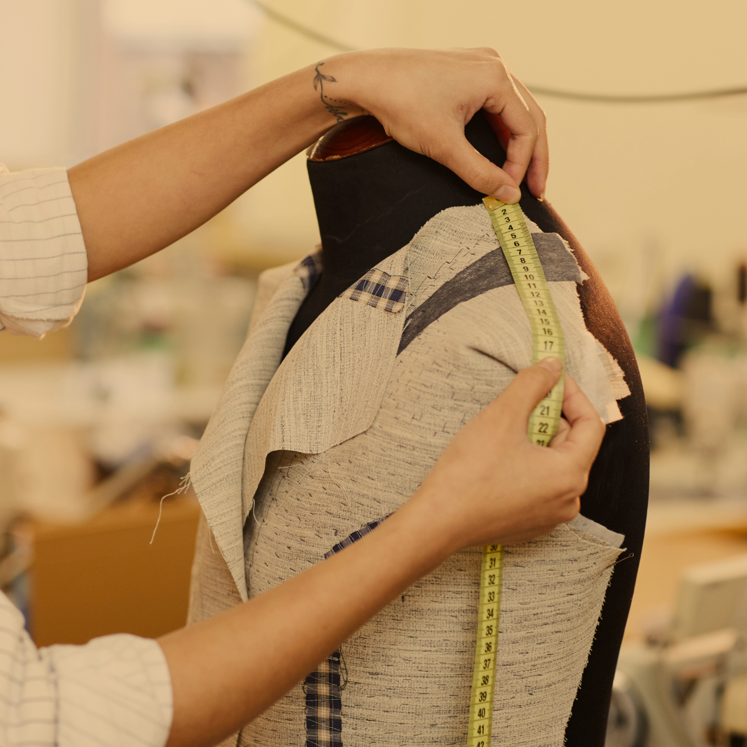 Person's shoulder fitting of fabric while measuring with a tape measure in a tailoring or fashion design setting.