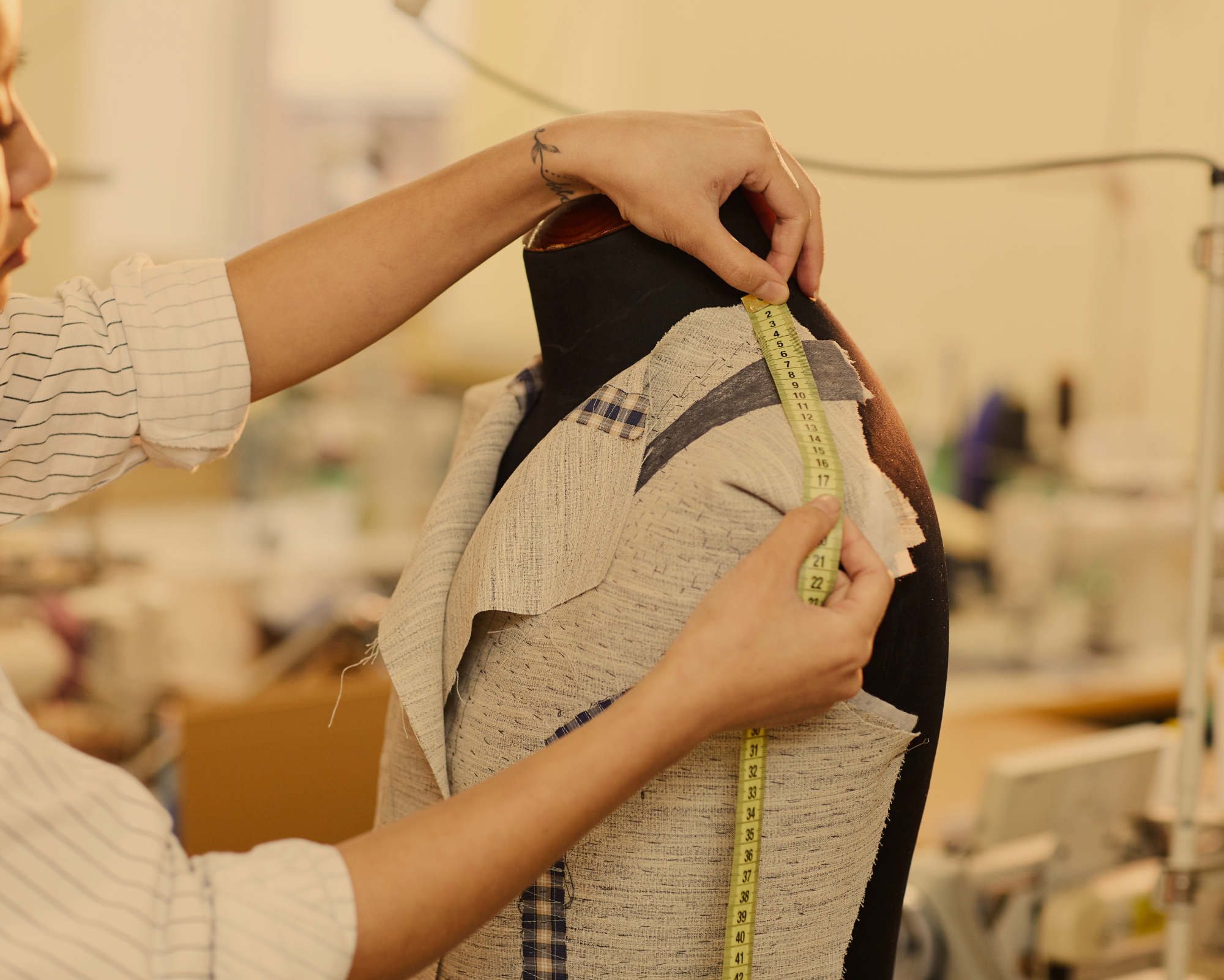 A person measures the shoulder of a mannequin with a tape measure.