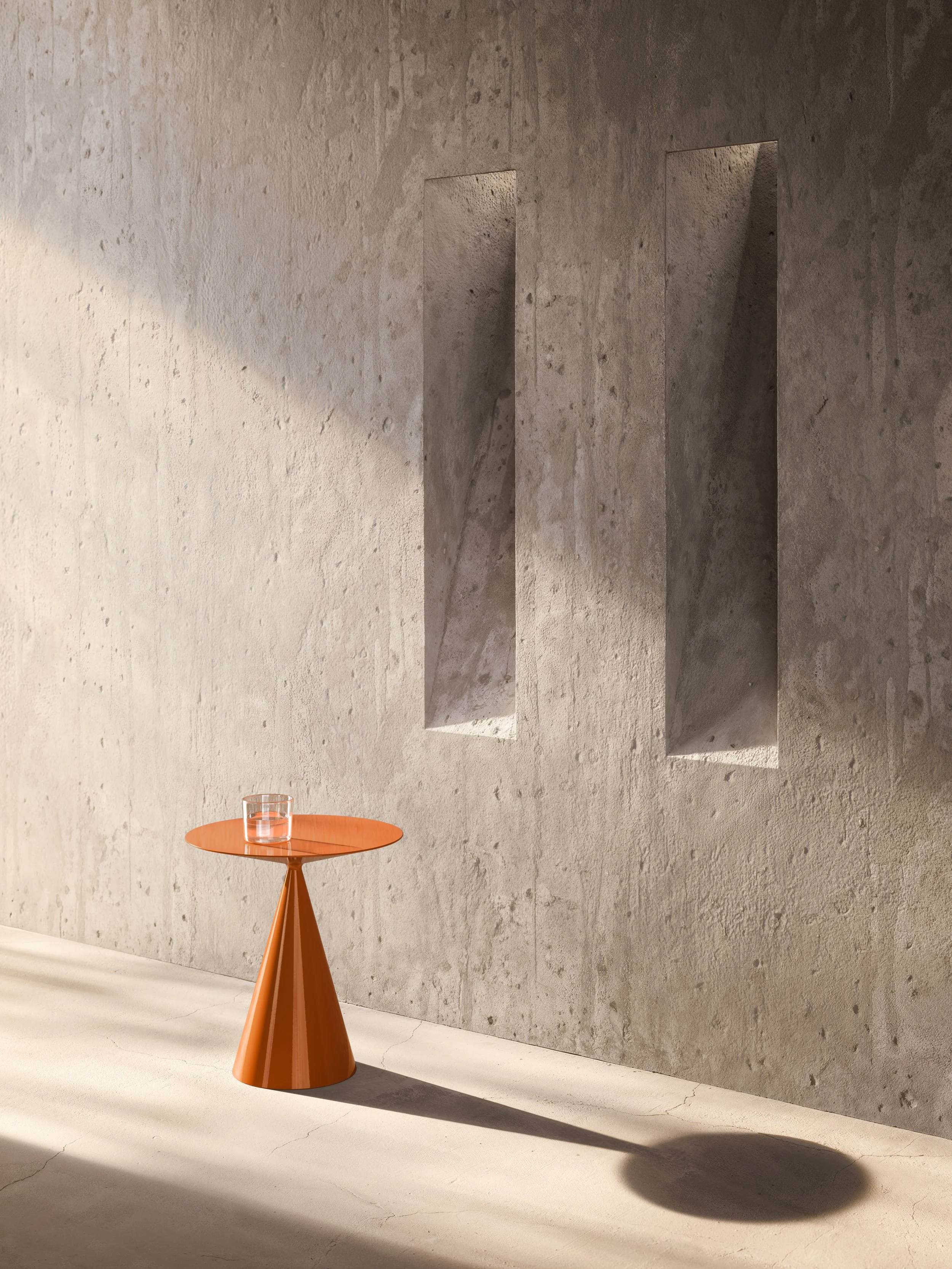 A small orange side table with a glass of water on it, placed against a textured concrete wall with two narrow rectangular cutouts, casting a shadow on the floor.